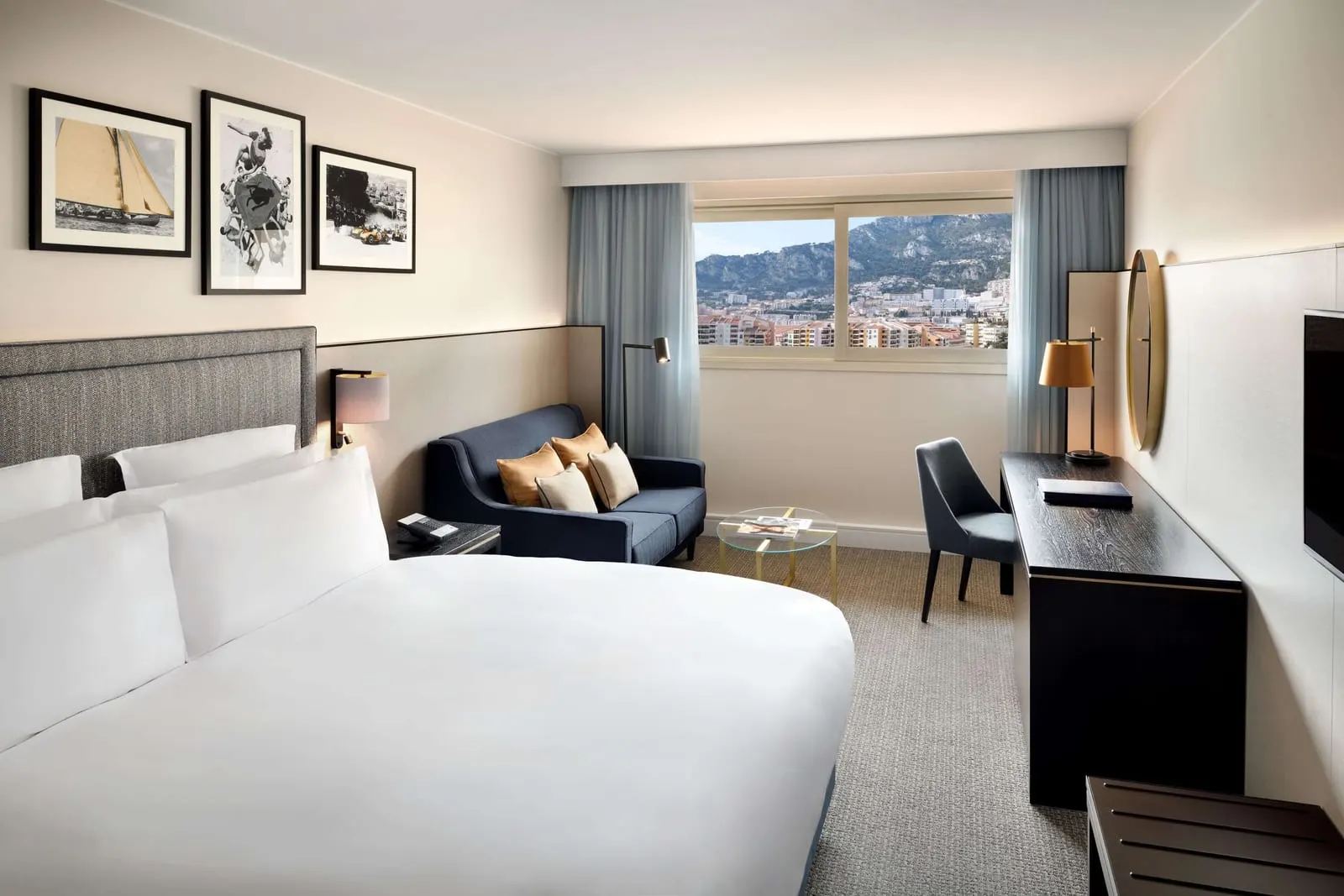 Superior Room at Columbus Hotel Monte-Carlo: the bed, a blue sofa, a desk and a window over the town and the hills