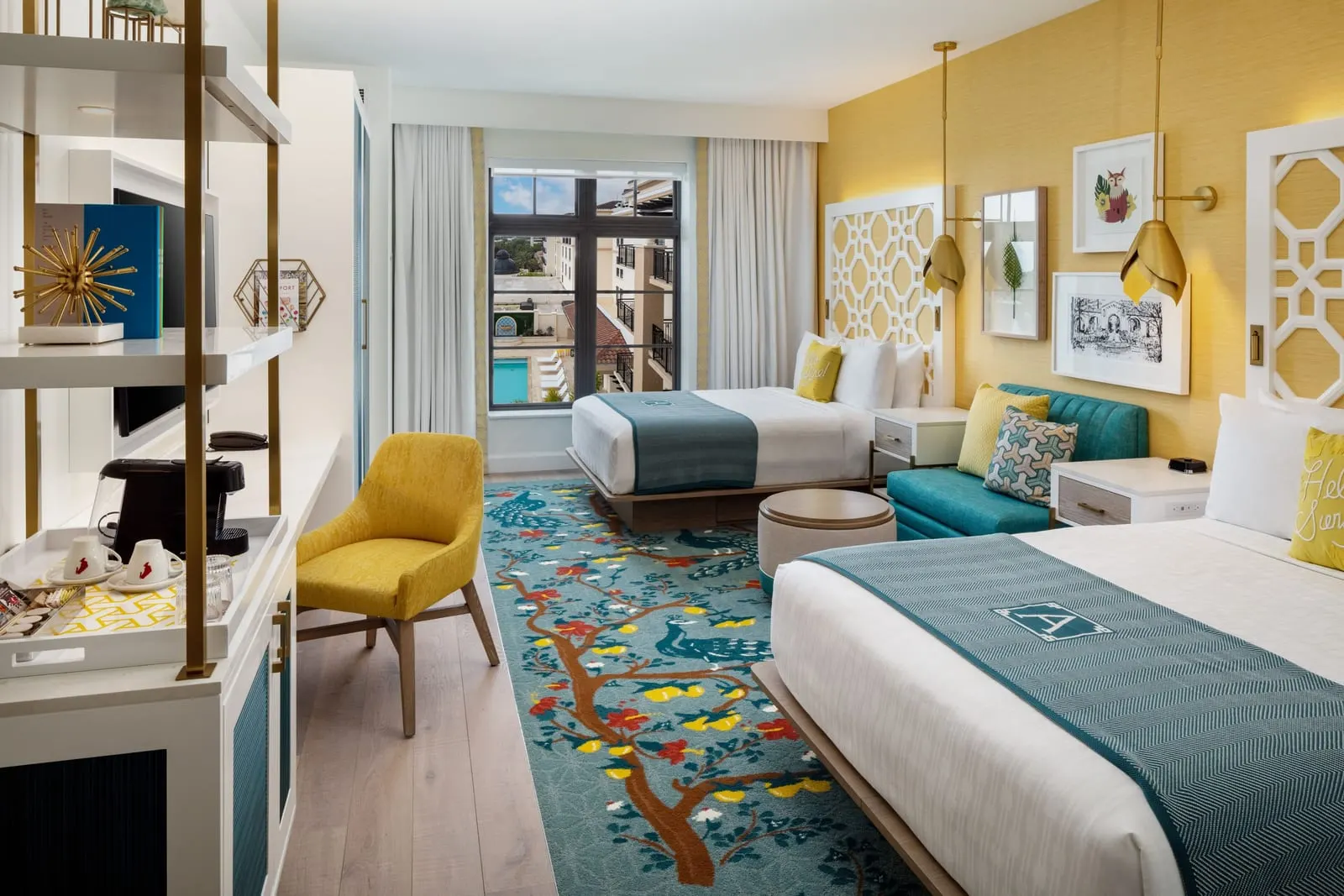 Classic Queen at The Alfond Inn: two queen beds on a peacock-patterned rug, a small teal settee with a round ottoman, a yellow chair and open shelving with a coffee machine