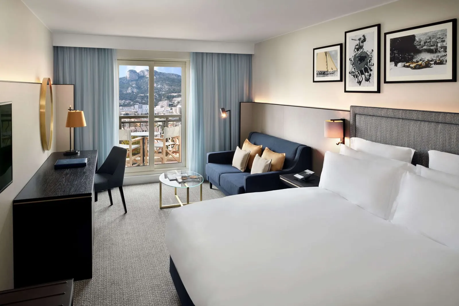 Deluxe Room at Columbus Hotel Monte-Carlo: the bed, a blue sofa and a window onto a balcony over the town