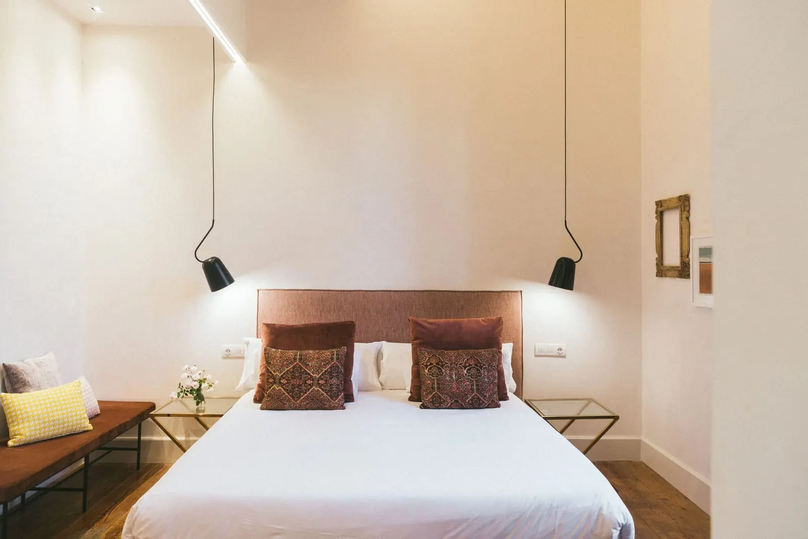 Premium at Hotel Veintiuno: a king bed with a terracotta headboard between two black pendant lamps, with glass bedside tables and a cushioned bench on a wooden floor