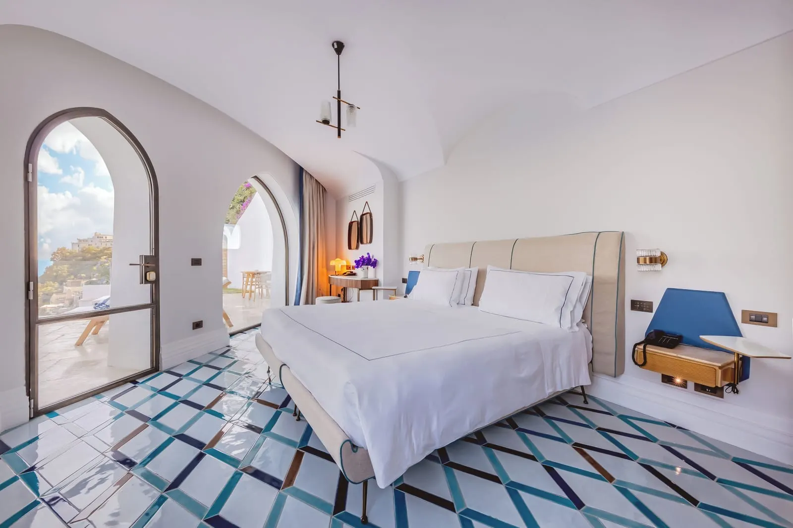 Premium Suite Sea View & Pool at Borgo Santandrea: a king bed on a patterned tiled floor, with an arched glass door to the terrace.