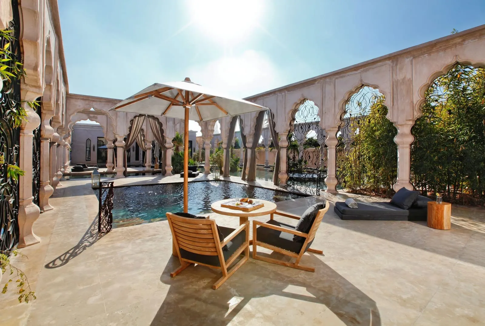 Pool Suite at Palais Namaskar: a terrace with a private pool, a parasol and armchairs inside a ring of carved arches