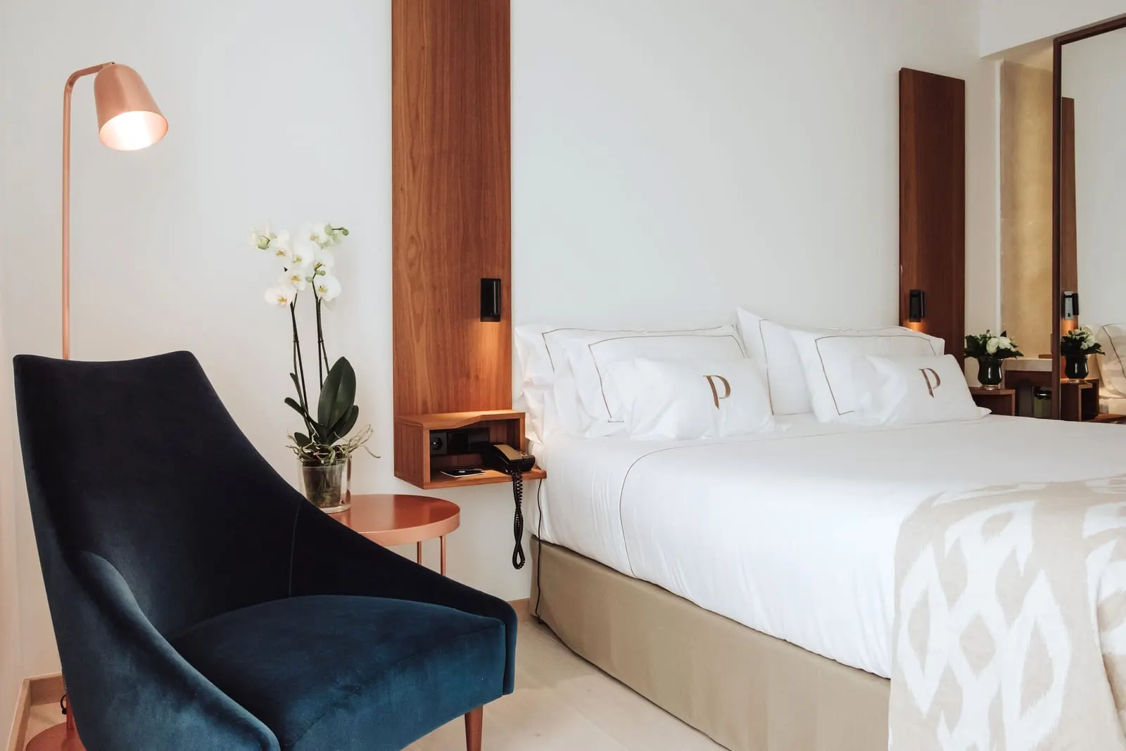 Deluxe Lateral Sea View at Es Princep: a double bed with monogrammed pillows beside a blue velvet armchair, a copper floor lamp and an orchid