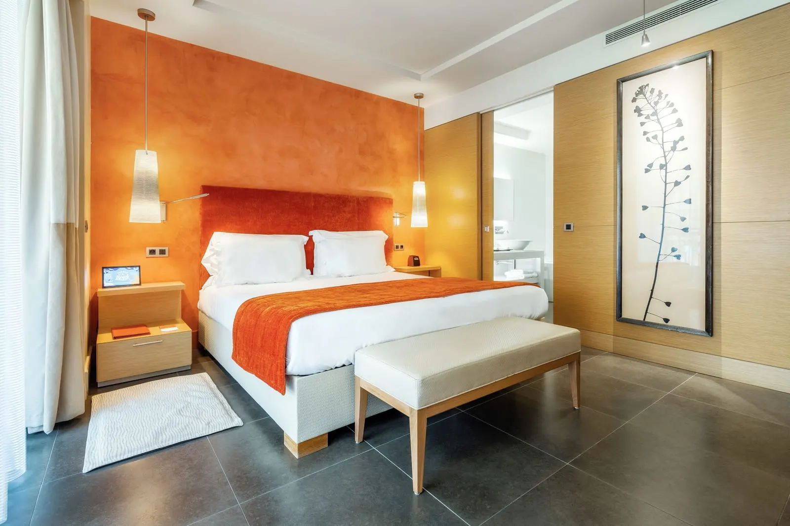 Deluxe Room with city view at Monte-Carlo Bay Hotel & Resort: the bed against an orange wall, with a bench at its foot