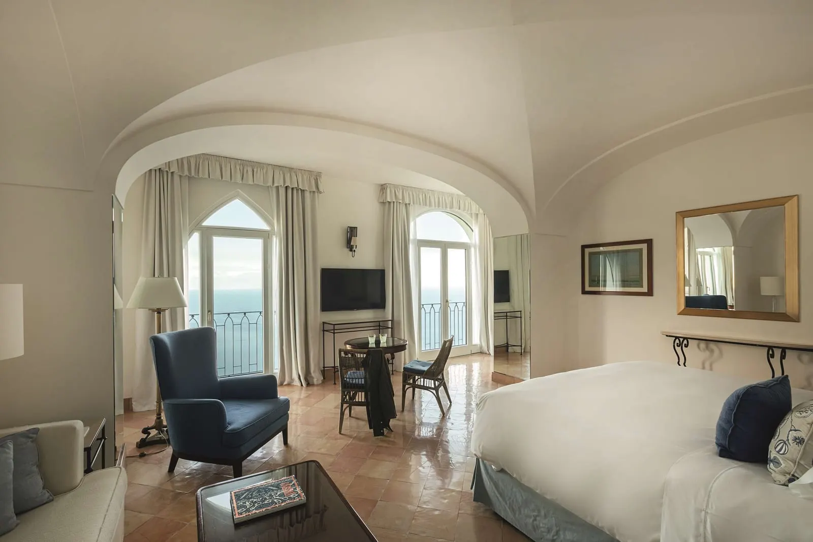 Deluxe Sea View Junior Suite with Balcony at Caruso, A Belmond Hotel: a bed, an armchair and a small table under a vaulted ceiling, with two glass doors onto balconies over the sea