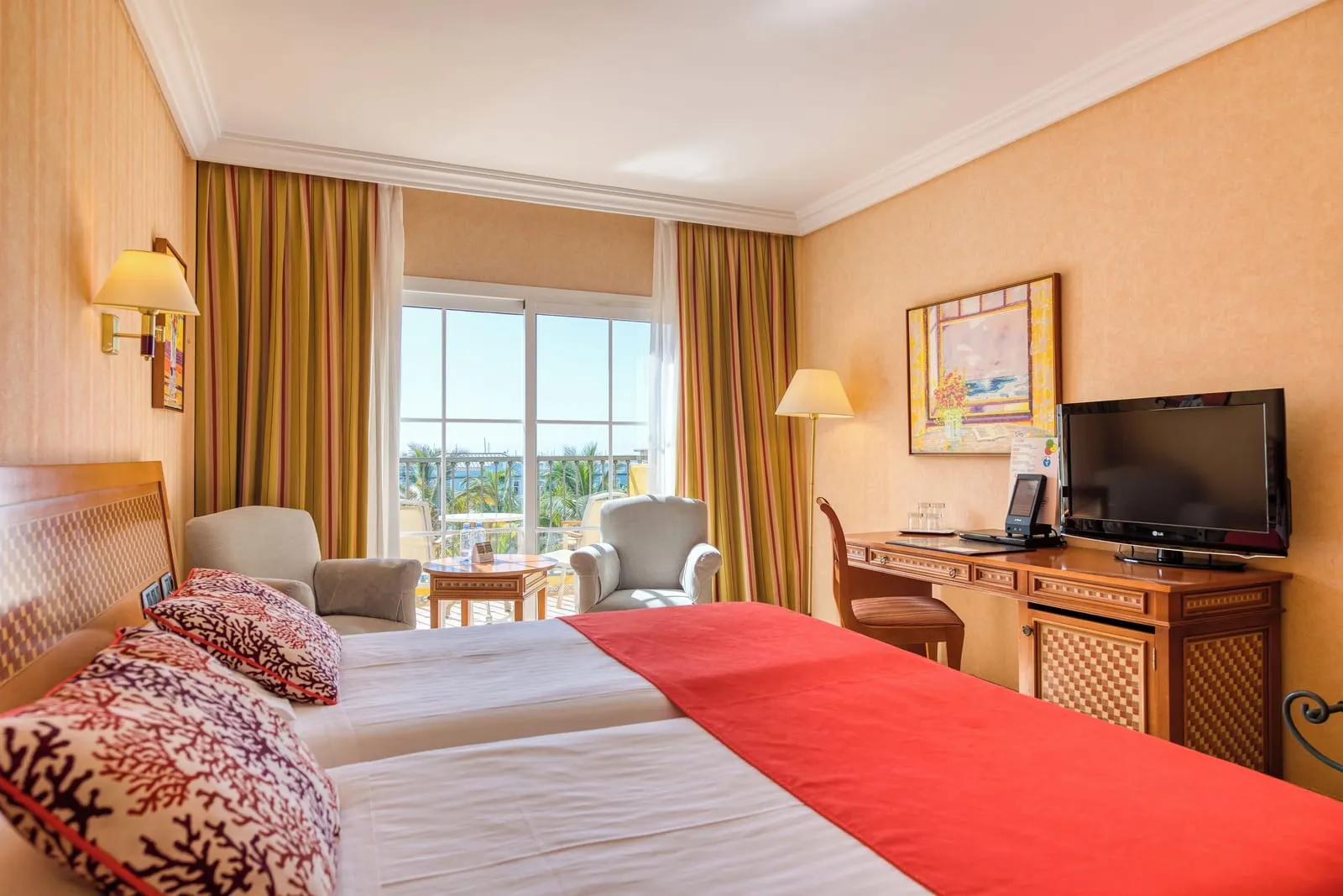 Double Room at Hotel Cordial Mogán Playa: two single beds side by side, two armchairs by glass doors to the balcony and a desk with a television