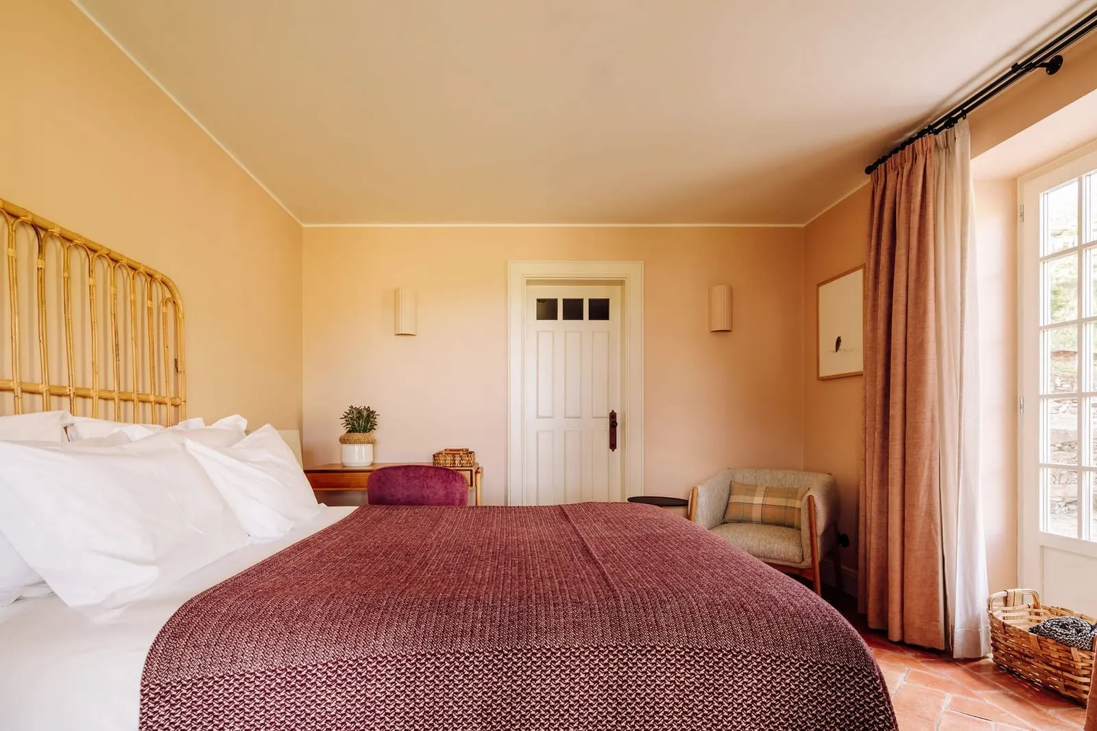 Terrace Accommodation at Quinta Nova: the bed with a rattan headboard, an armchair, a terracotta floor and glazed doors