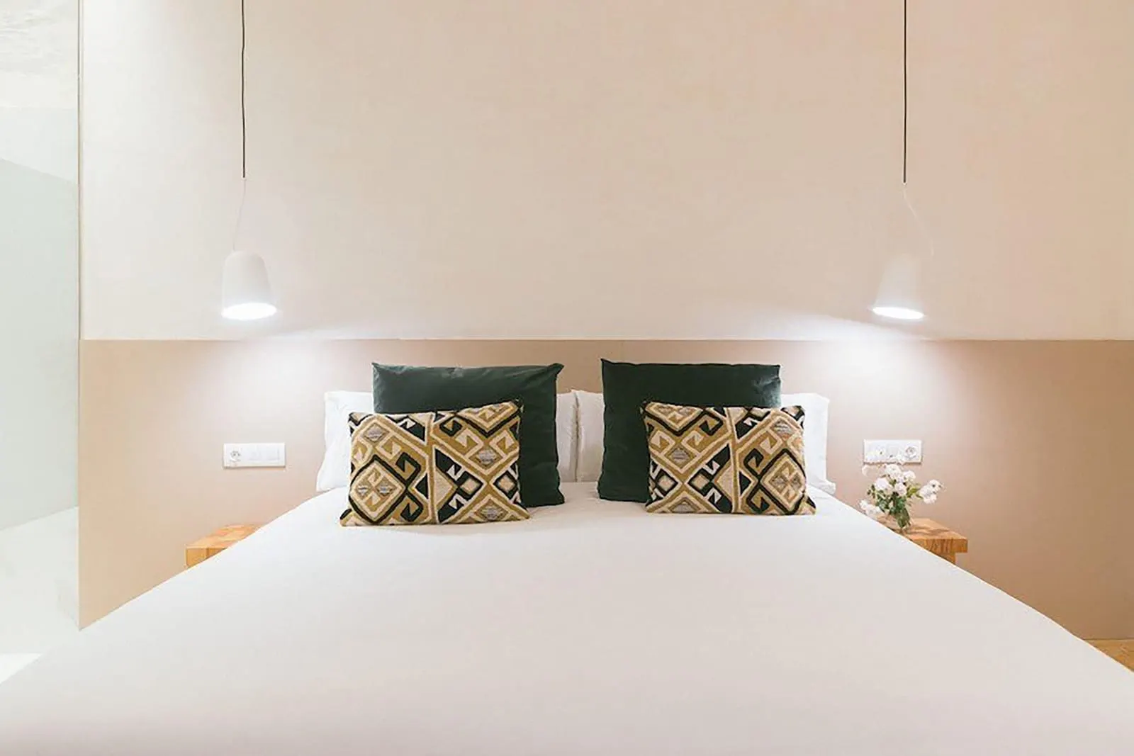 Classic Interior at Hotel Veintiuno: a double bed with dark green and geometric cushions under two white pendant lamps, against a low beige headboard panel
