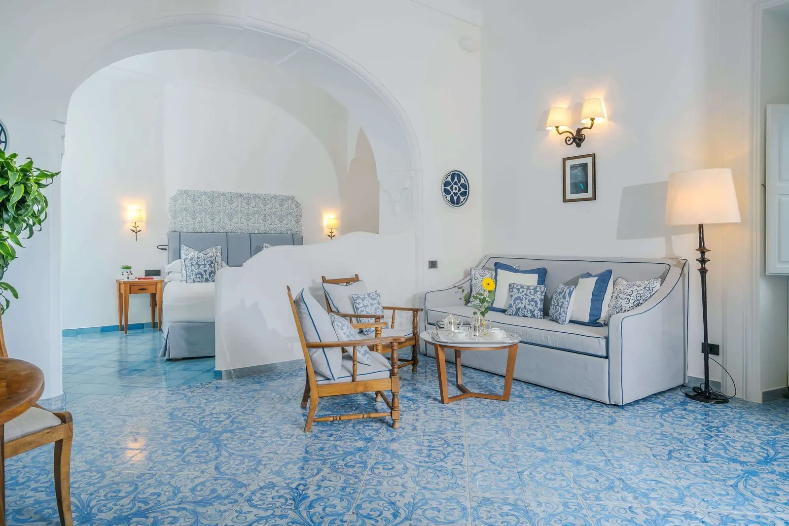 Suite with king size bed plus two extra single beds im Palazzo Murat: ein Bett hinter einem Bogen und eine Sitzecke mit einem Sofa auf einem blauen Majolikaboden