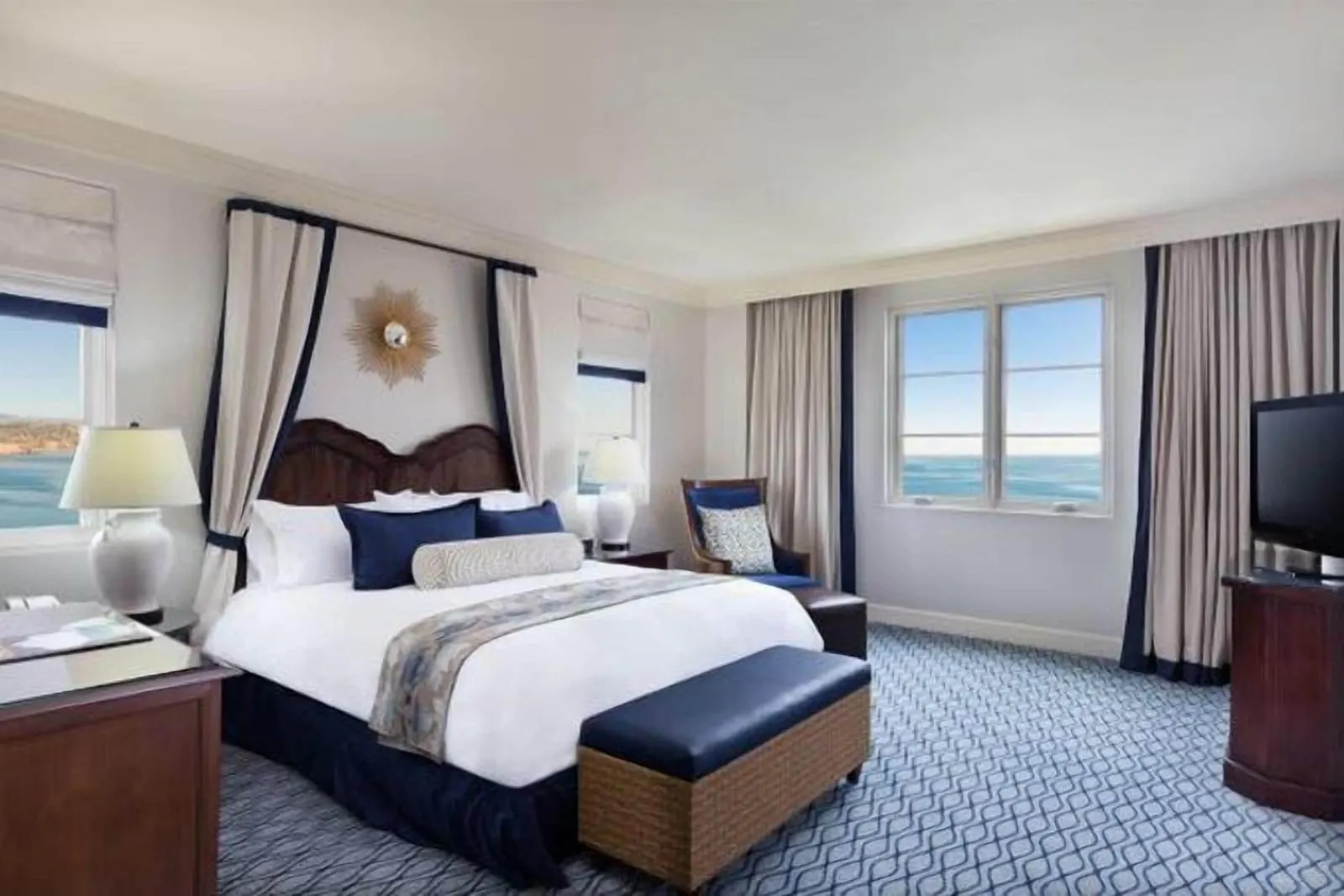 One-Bedroom Hotel Suite, Premier Ocean View at Terranea Resort: a bed beneath a navy-trimmed canopy with a blue bench at its foot, a television and corner windows