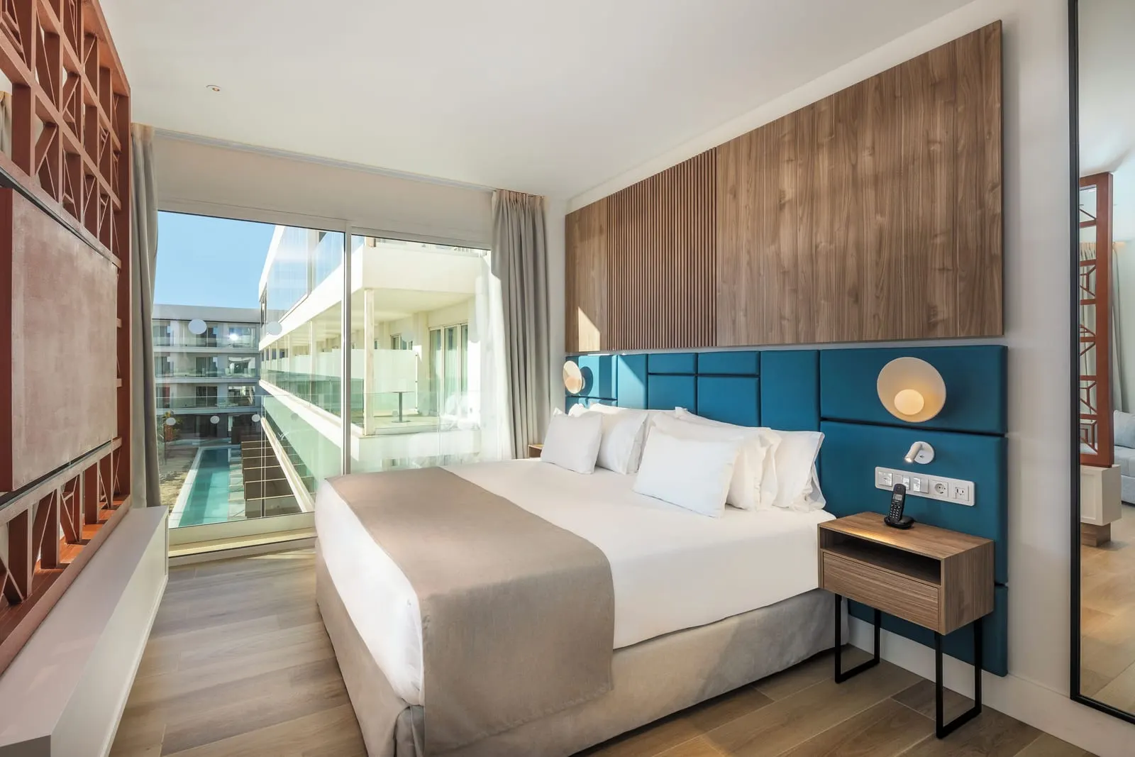 Junior Suite at Barceló Playa Blanca: a bed with a teal headboard and a timber panel, beside glass doors to the balcony