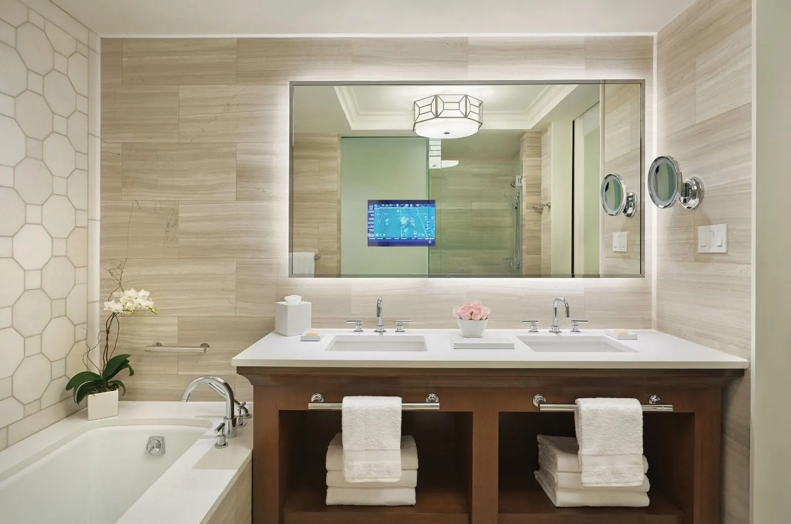 Park View Room im Four Seasons Resort Orlando at Walt Disney World Resort: ein Badezimmer mit einem Doppelwaschtisch, einem in den Spiegel eingelassenen Fernseher, einer Badewanne und einer verglasten Dusche, die im Spiegel zu sehen ist