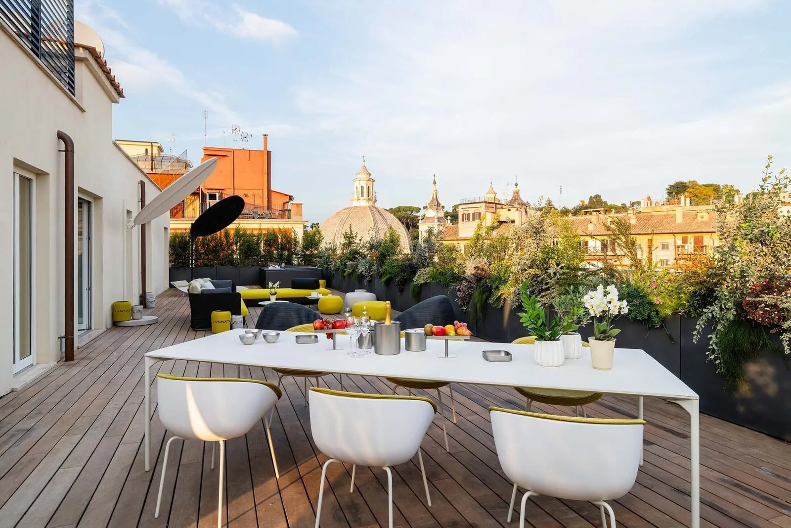 Penthouse at ROMEO Roma: the terrace with a long white table and chairs, planters and a dome on the skyline