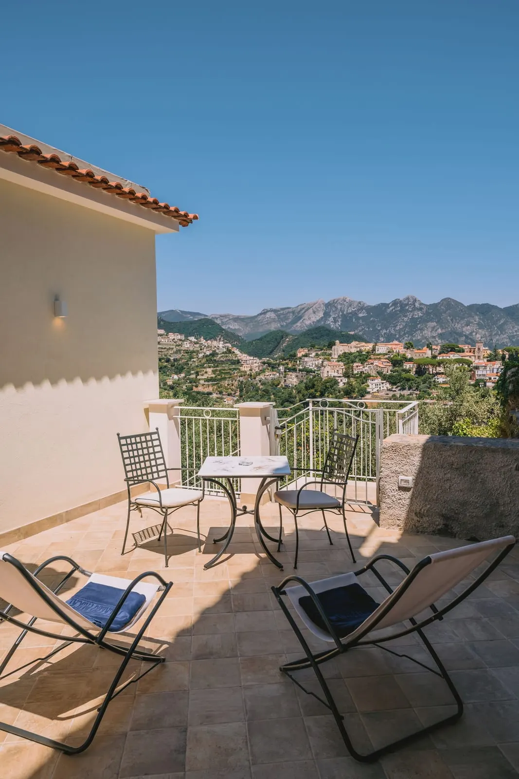 Deluxe Room SAMBUCO at Palazzo Pascal: a tiled terrace with two loungers, a table and chairs, looking over terraced hillsides to the mountains