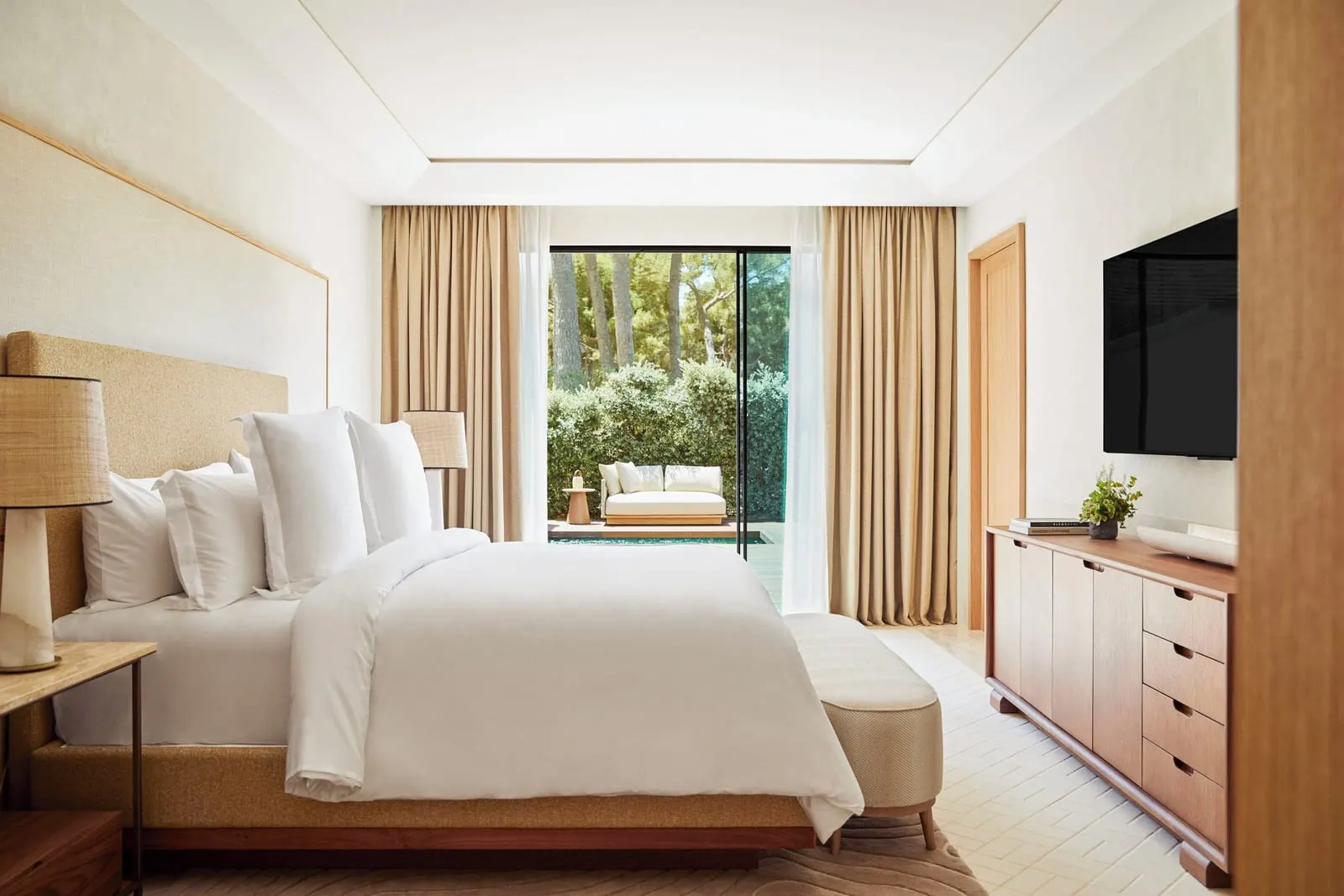 Garden-View Suite with Plunge Pool im Four Seasons Resort Mallorca at Formentor: ein Kingsize-Bett mit einer gepolsterten Bank, eine Holzkommode und ein Fernseher, mit Glastüren zu einer Terrasse mit einem Tagesbett und einem Tauchbecken