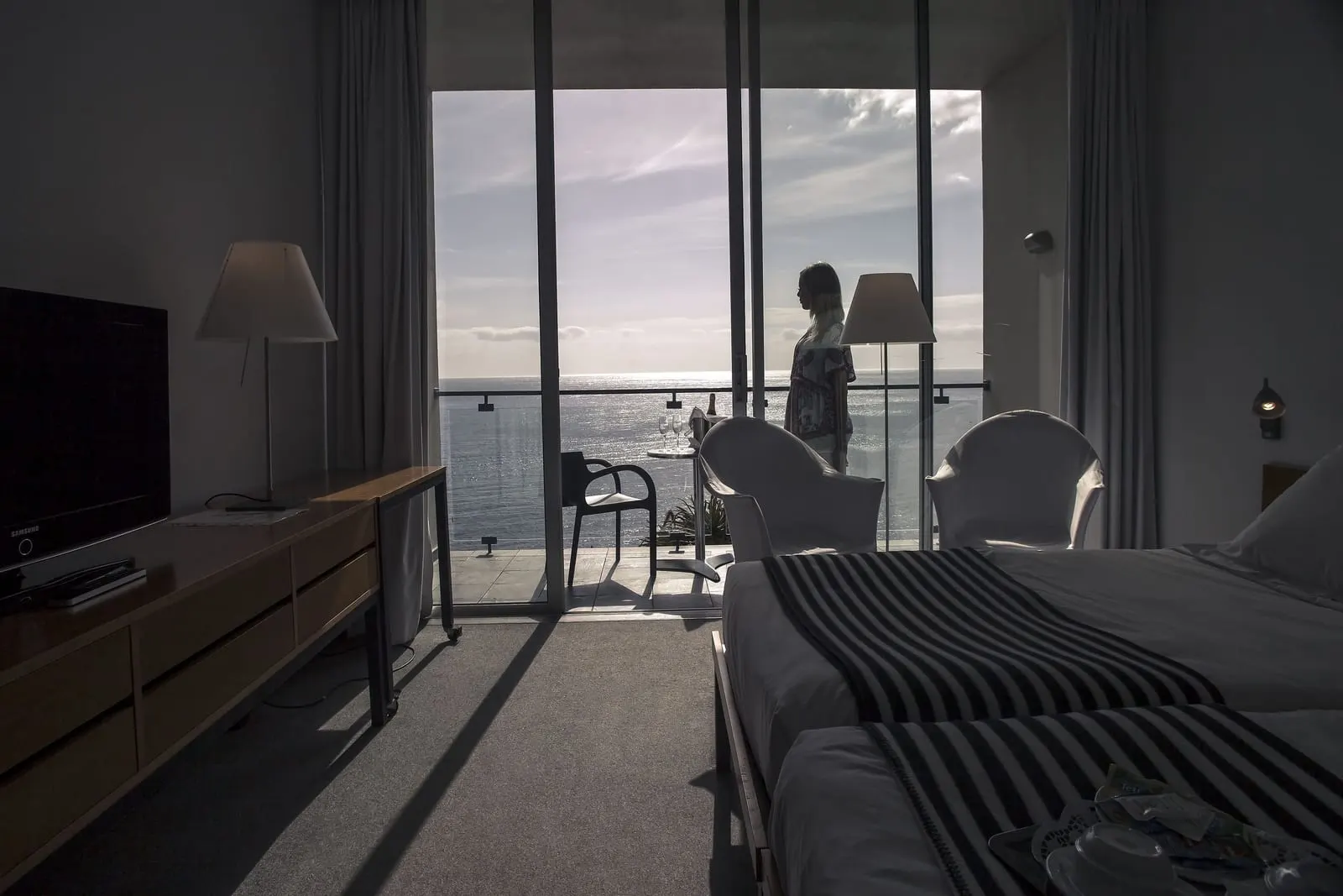 Estalagem Double Sea View in der Estalagem da Ponta do Sol: ein Schreibtisch mit Fernseher und Lampe gegenüber den Betten, mit offenen Glastüren zu einem Balkon über dem Meer