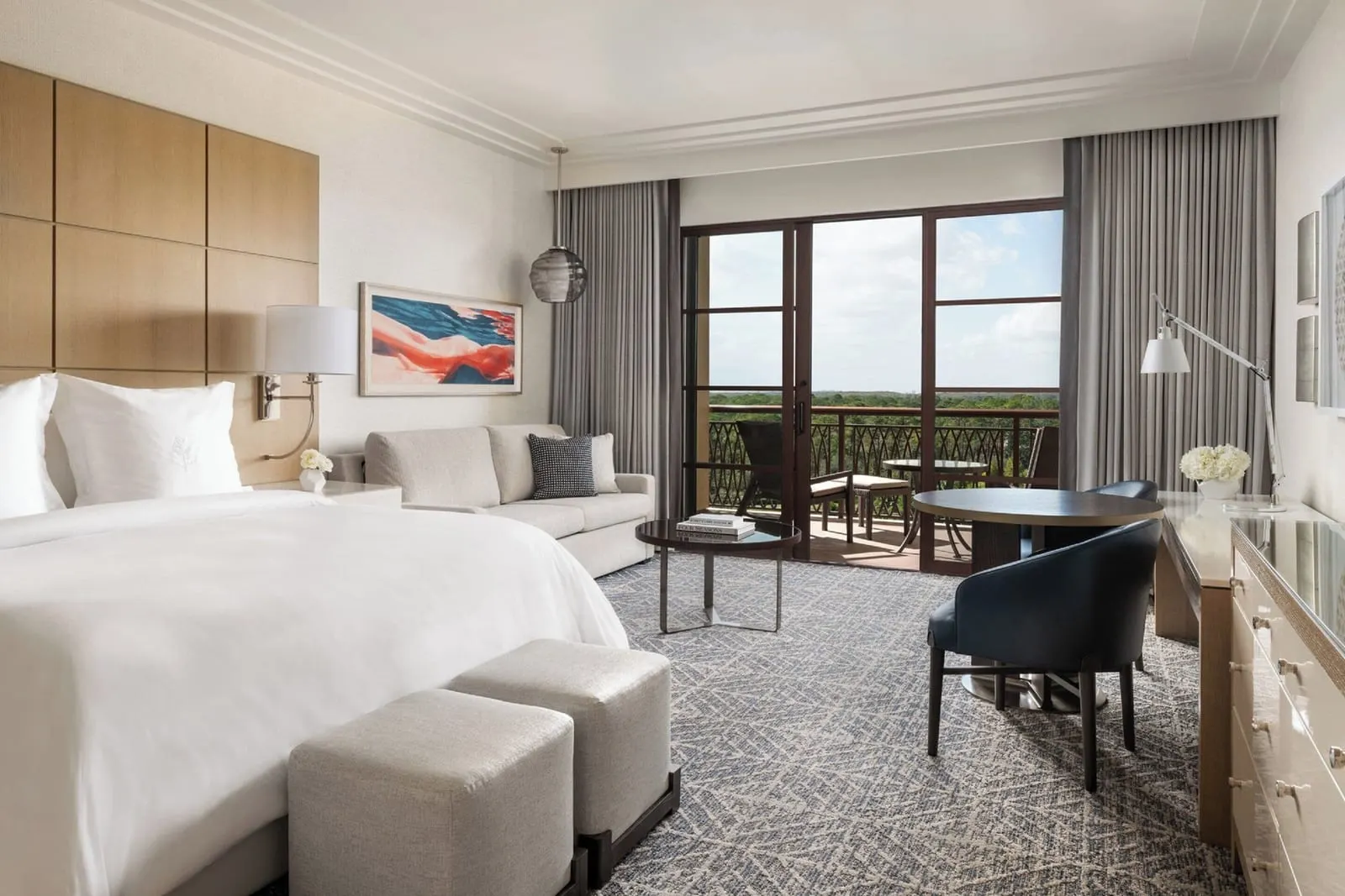 Park View Room at Four Seasons Resort Orlando at Walt Disney World Resort: a king bed, a sofa, a round table with two chairs and glass doors onto a terrace set with a table and chairs