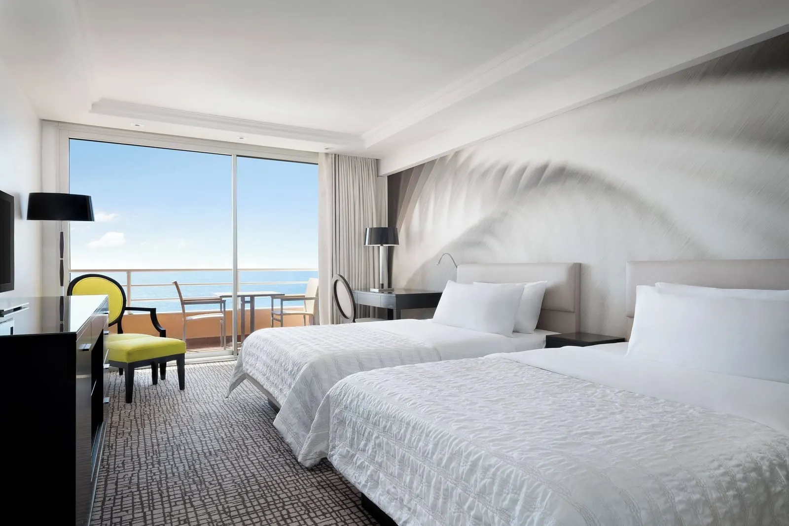 Deluxe sea-view room at Le Méridien Beach Plaza with two double beds, a yellow armchair and a window onto the sea