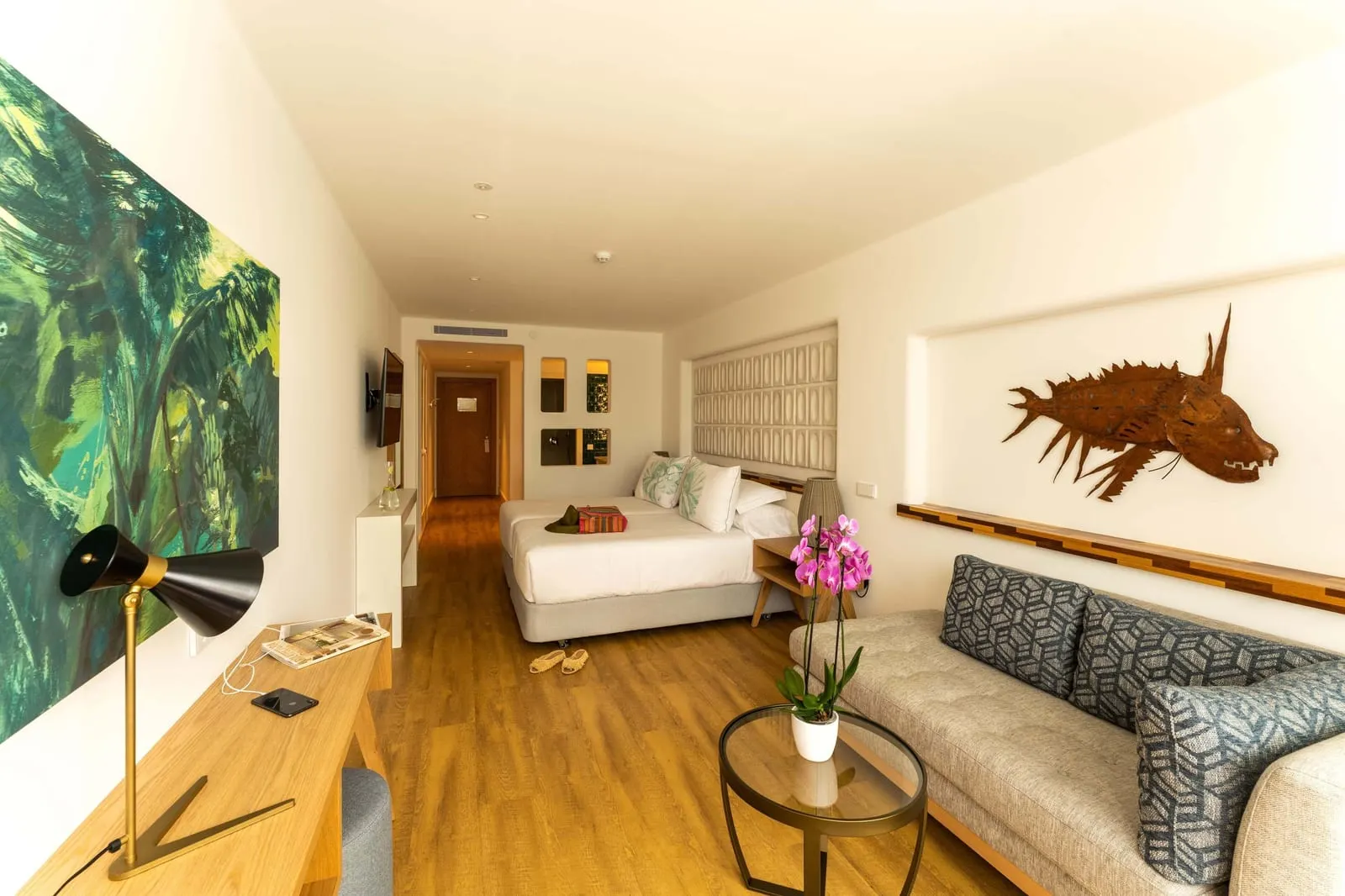 Junior Suite Relax Sea View at Hotel Fariones: a long room with a bed at the far end and a sofa and low table in front of a large painting