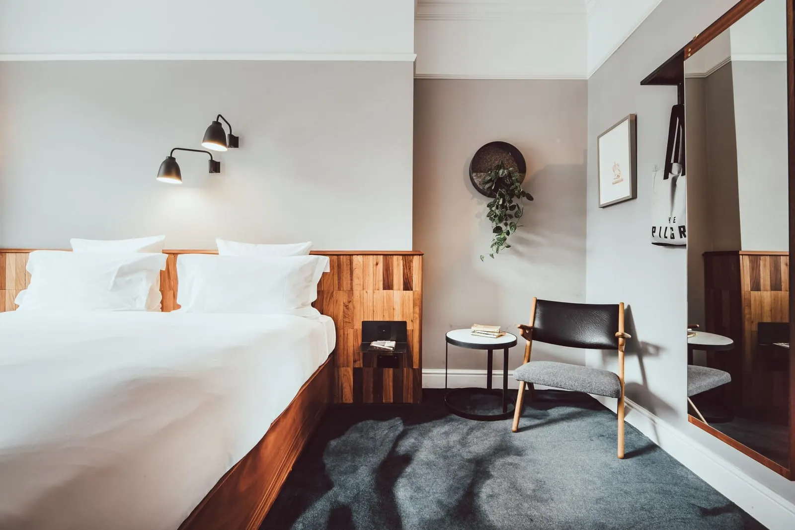 Comfy room at The Pilgrm: the bed with a wood headboard, a leather chair, a small round table and a long mirror