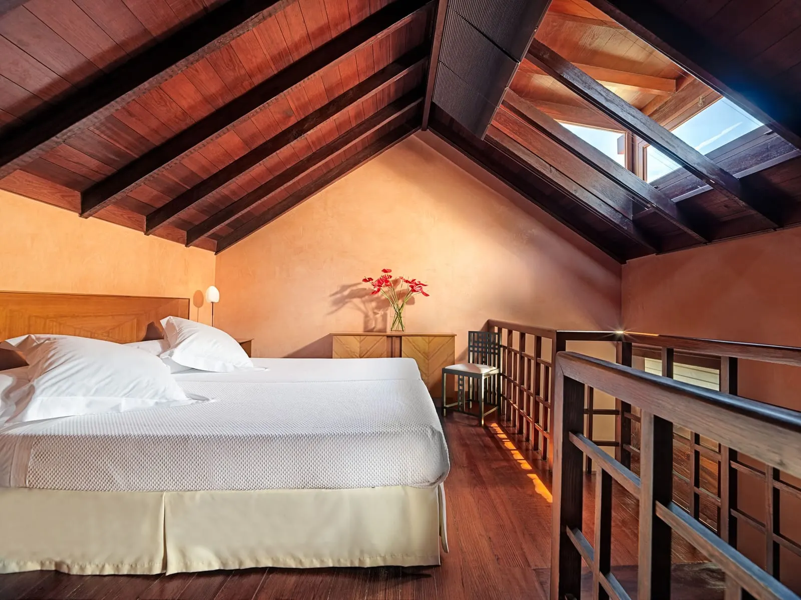 Dúplex at Hotel San Roque: the upstairs bedroom under a sloping timber roof, with a skylight and a wooden balustrade