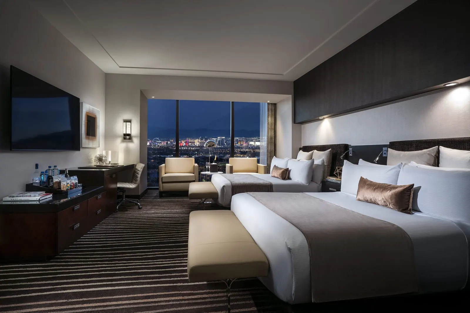 Signature Suite Two Queens at Red Rock Casino Resort & Spa: two queen beds with an upholstered bench at the foot of each, two armchairs by a floor-to-ceiling window, and a desk and dresser below a wall-mounted television