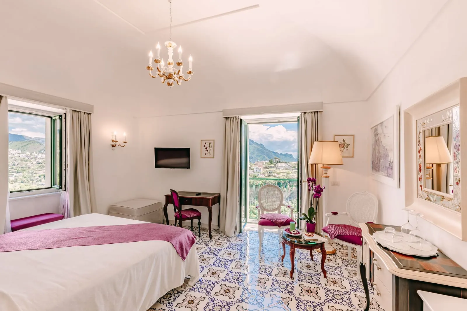 Grand Deluxe Suite ROSA CANINA at Palazzo Pascal: a double bed facing a sitting area with a desk, under a chandelier, with two open French windows