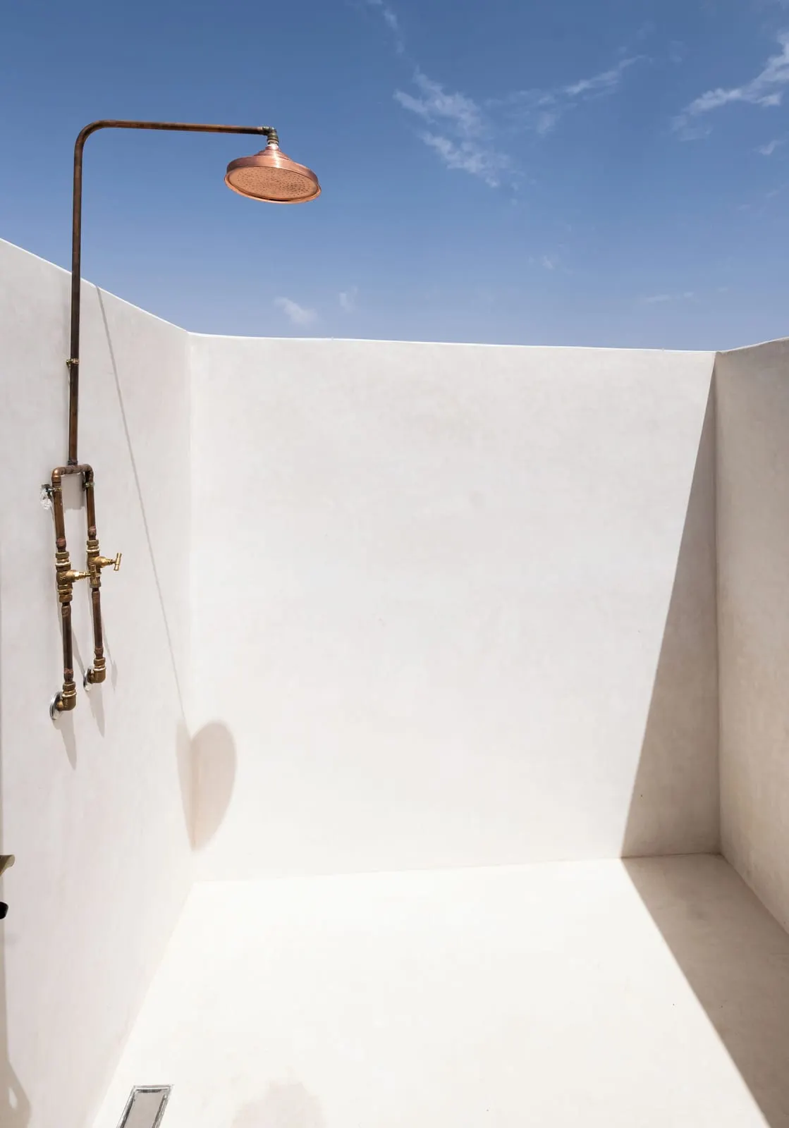 Emotion Suite at Inara Camp: an outdoor shower with a brass rain head in a white walled enclosure open to the sky.
