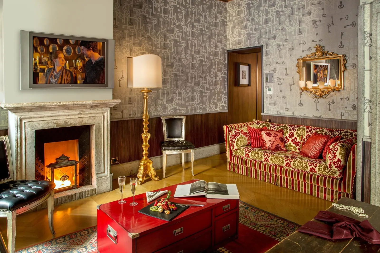 Junior Suite at The Inn at the Roman Forum: a sitting area with a lit fireplace, a striped sofa and a red chest
