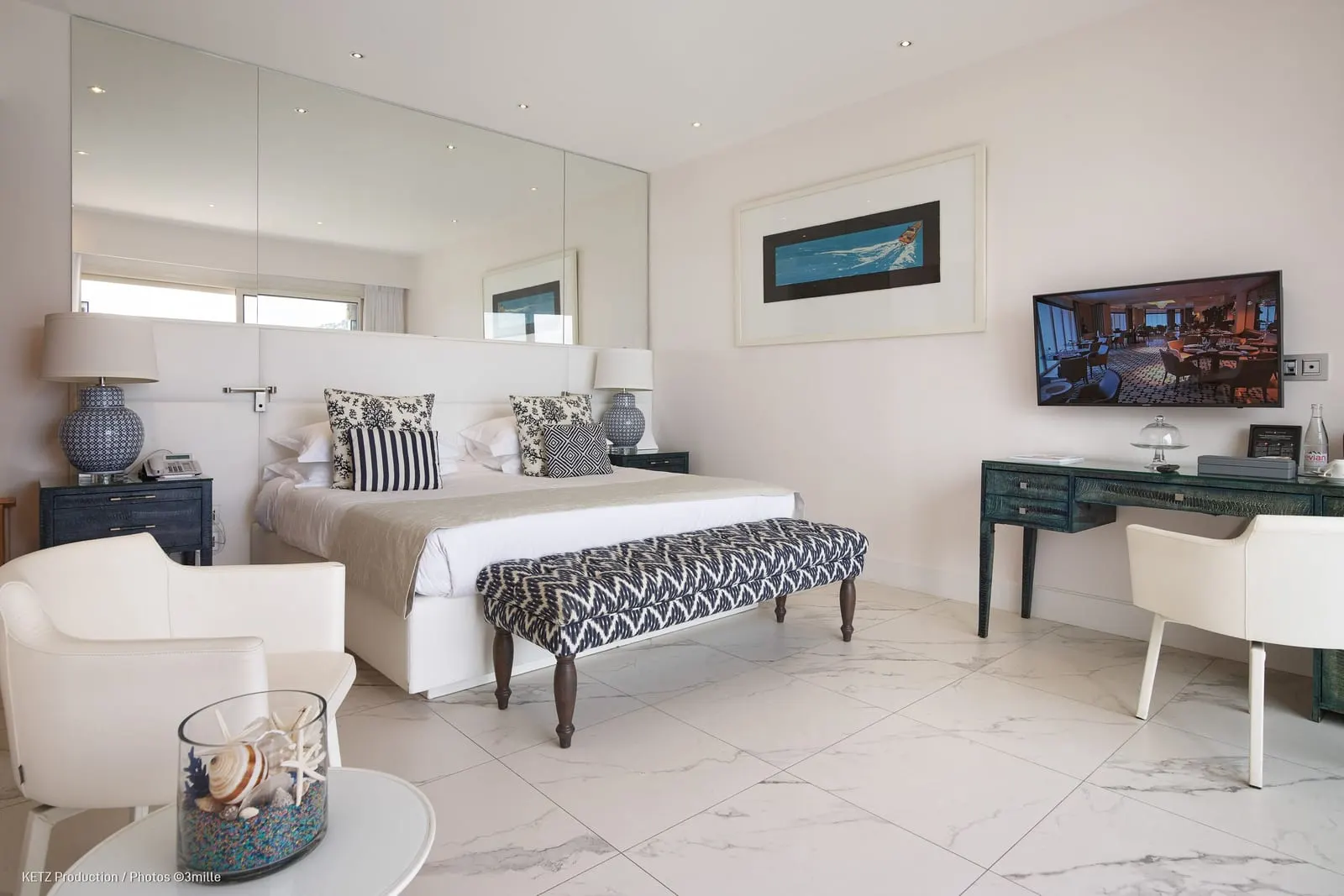 La Mer Deluxe Room at Cap Estel: the bed with a patterned bench, a desk and a wall-mounted television