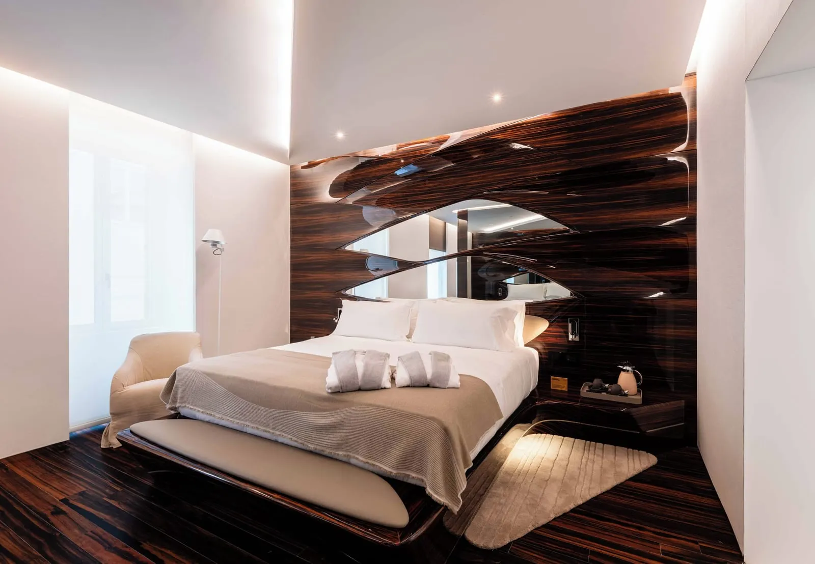 Premier Wellness Suite at ROMEO Roma: the bed below a carved ebony headboard, an armchair beside it
