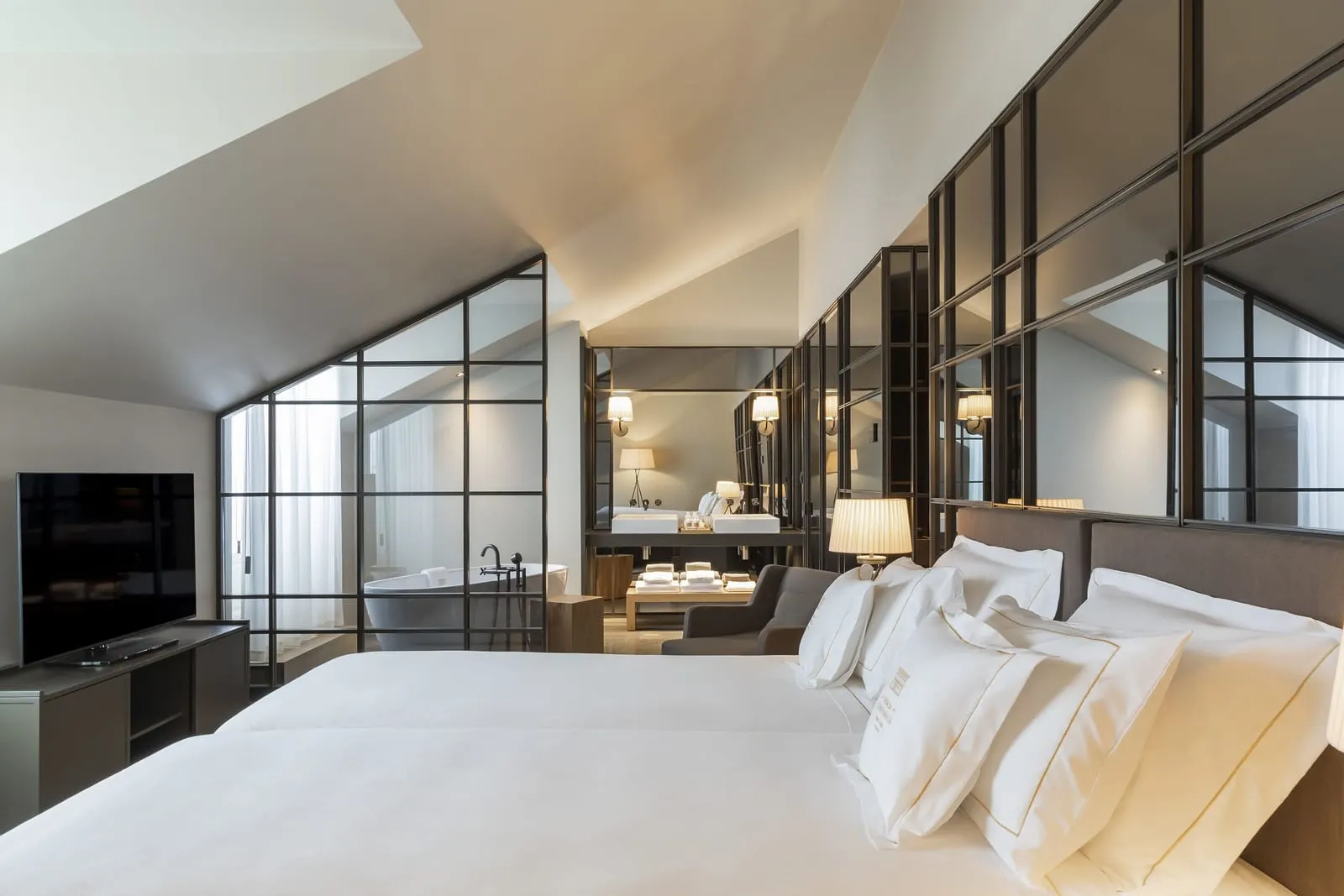 Twin Suite at Casa da Companhia: two beds under a sloping ceiling, a television and a glass wall onto the bathroom