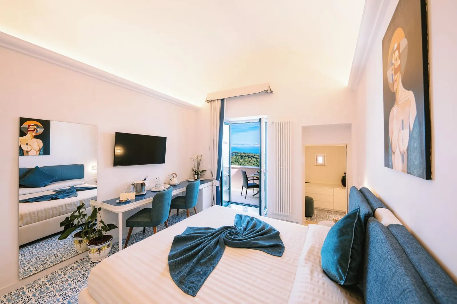 Premium Suite ANGELICA at Palazzo Pascal: a double bed with a blue headboard facing a desk and a glass door open onto the terrace