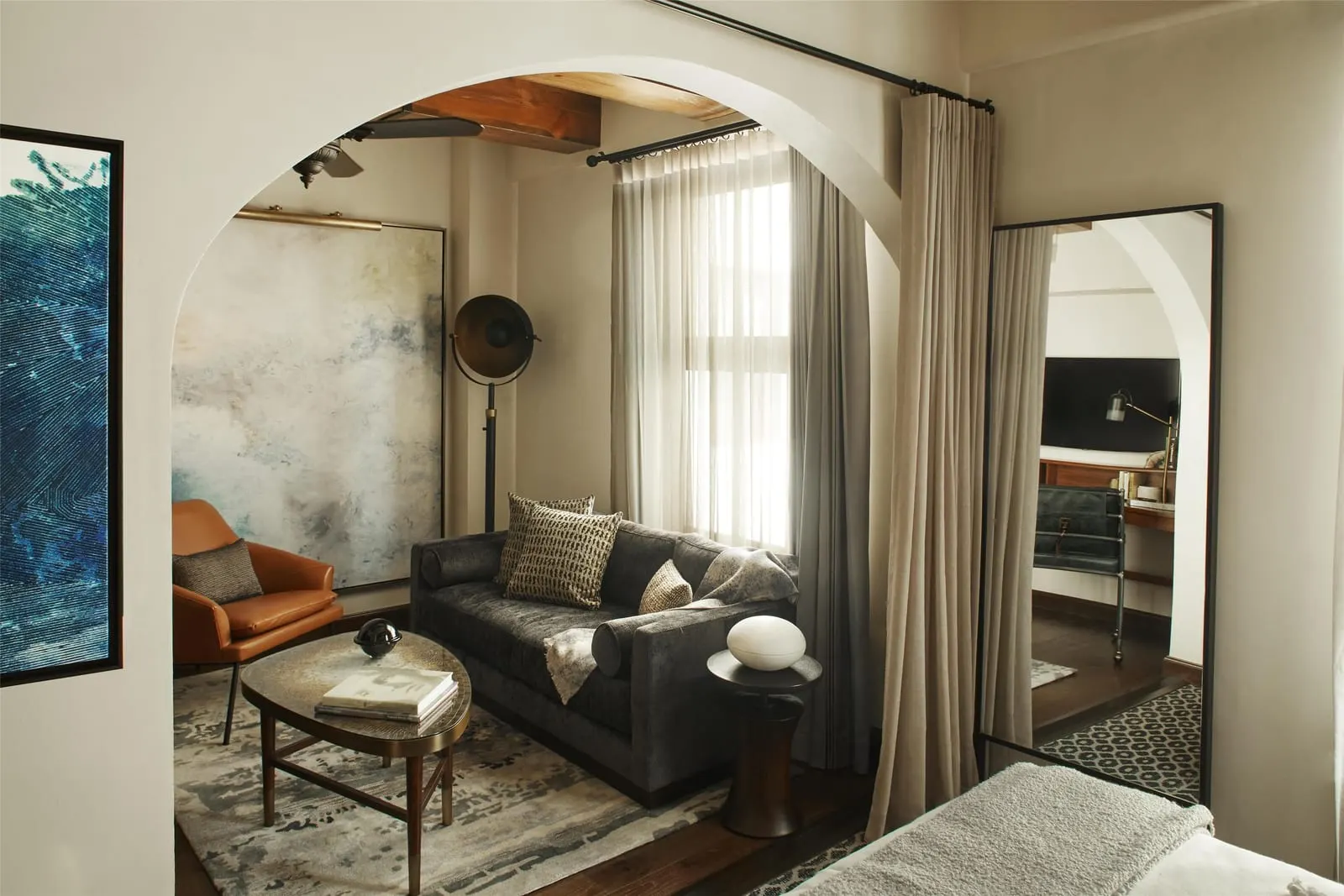 Junior Suite with 1 King Bed im Hotel Figueroa: ein Bogendurchgang zu einem Sitzbereich mit einem dunklen Sofa, einem hellbraunen Ledersessel und einem ovalen Couchtisch, mit der Ecke des Bettes im Vordergrund