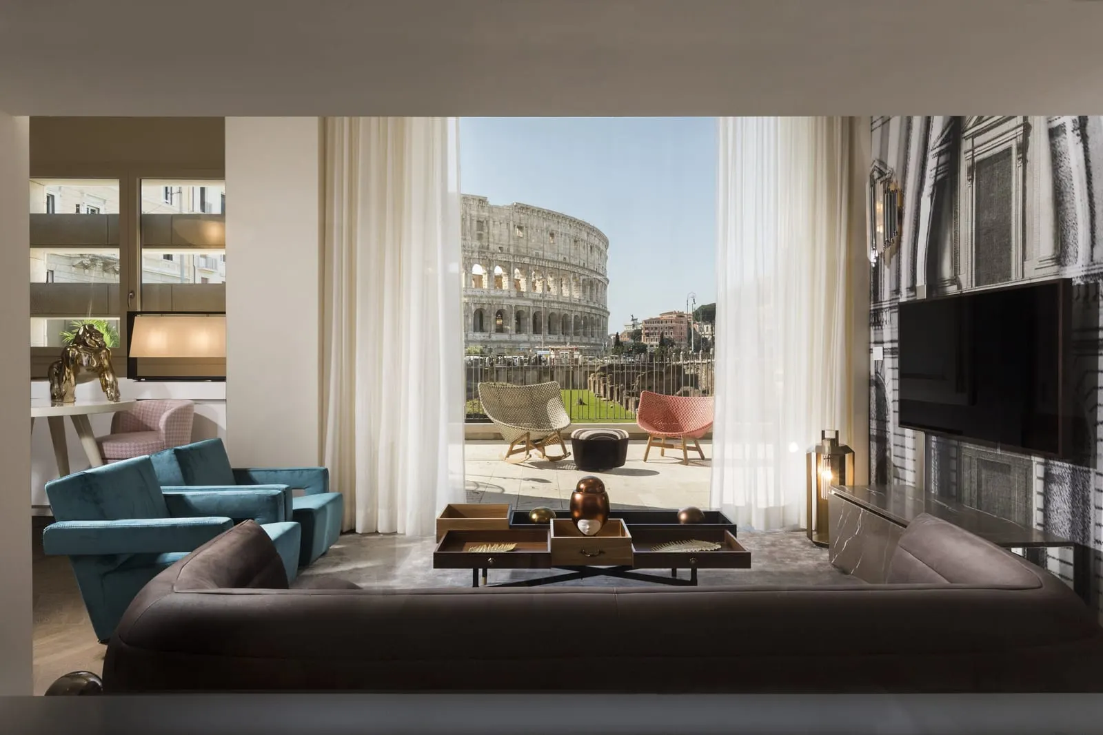 Grand View Suite Colosseo at Palazzo Manfredi: the living room, a sofa and blue armchairs, the Colosseum beyond the terrace