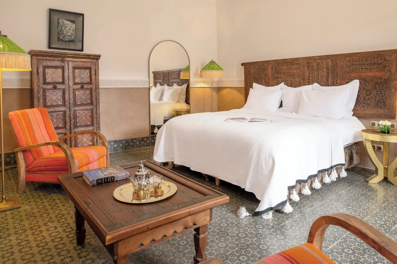 Private Riad at La Villa des Orangers: a double bed with a carved wooden headboard, orange armchairs and a tea tray on a low table.