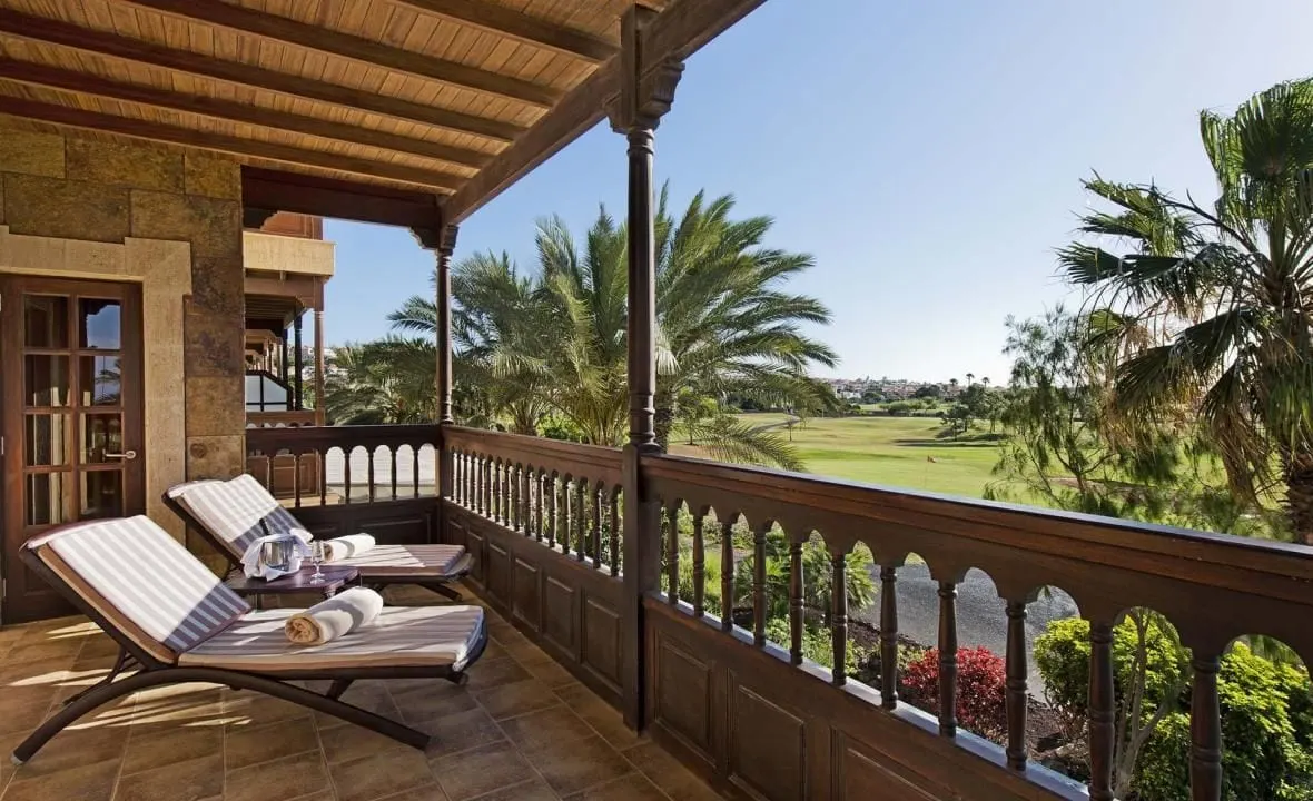 Suite with views of golf course at Elba Palace Golf Boutique Hotel: a covered wooden balcony with two loungers looking over palm trees to a fairway and green