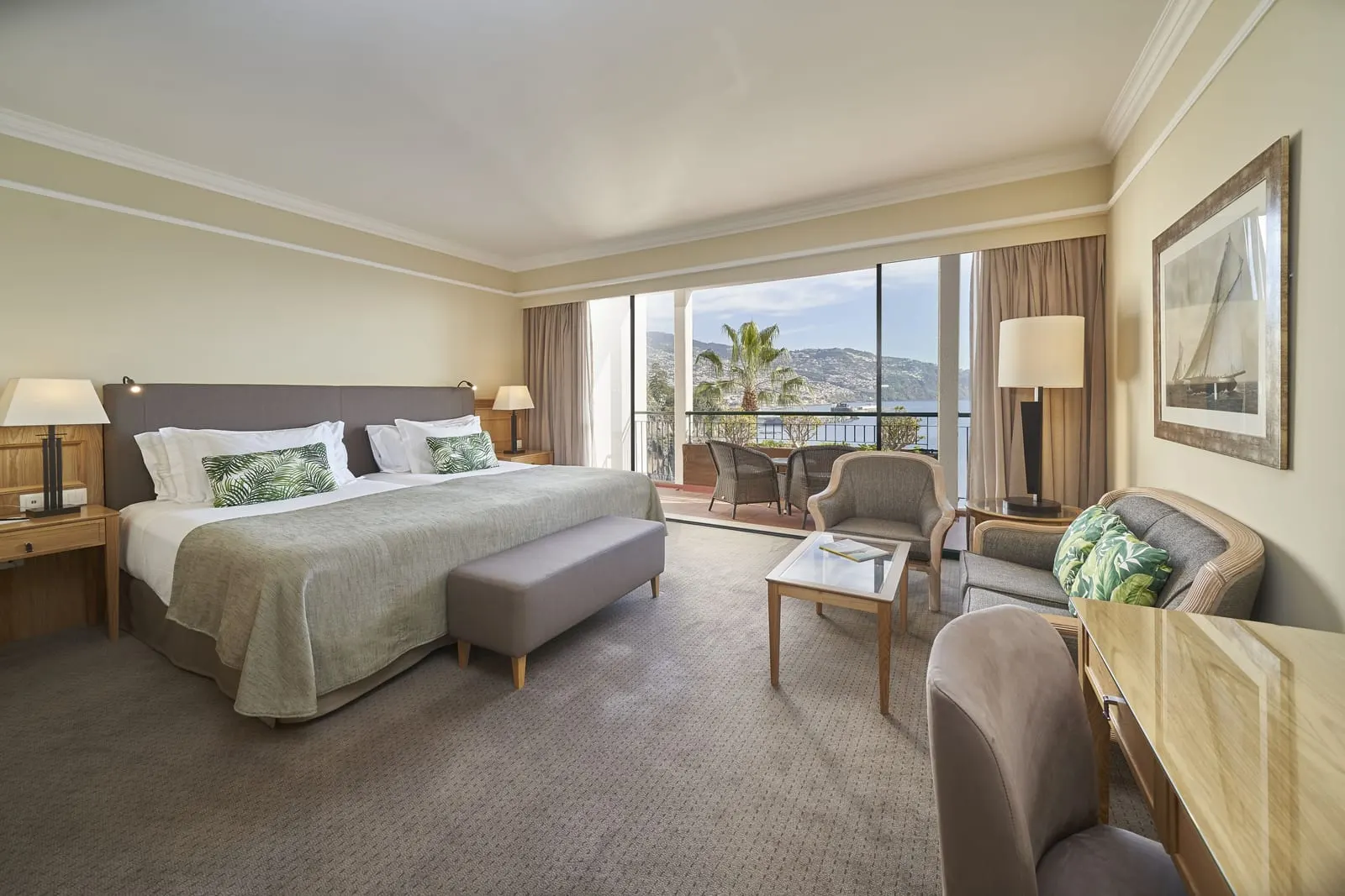 Funchal Bay View at The Cliff Bay, by PortoBay: twin beds made up as one, a sofa and armchair, and a balcony with wicker chairs looking across the harbour to Funchal on its hillside
