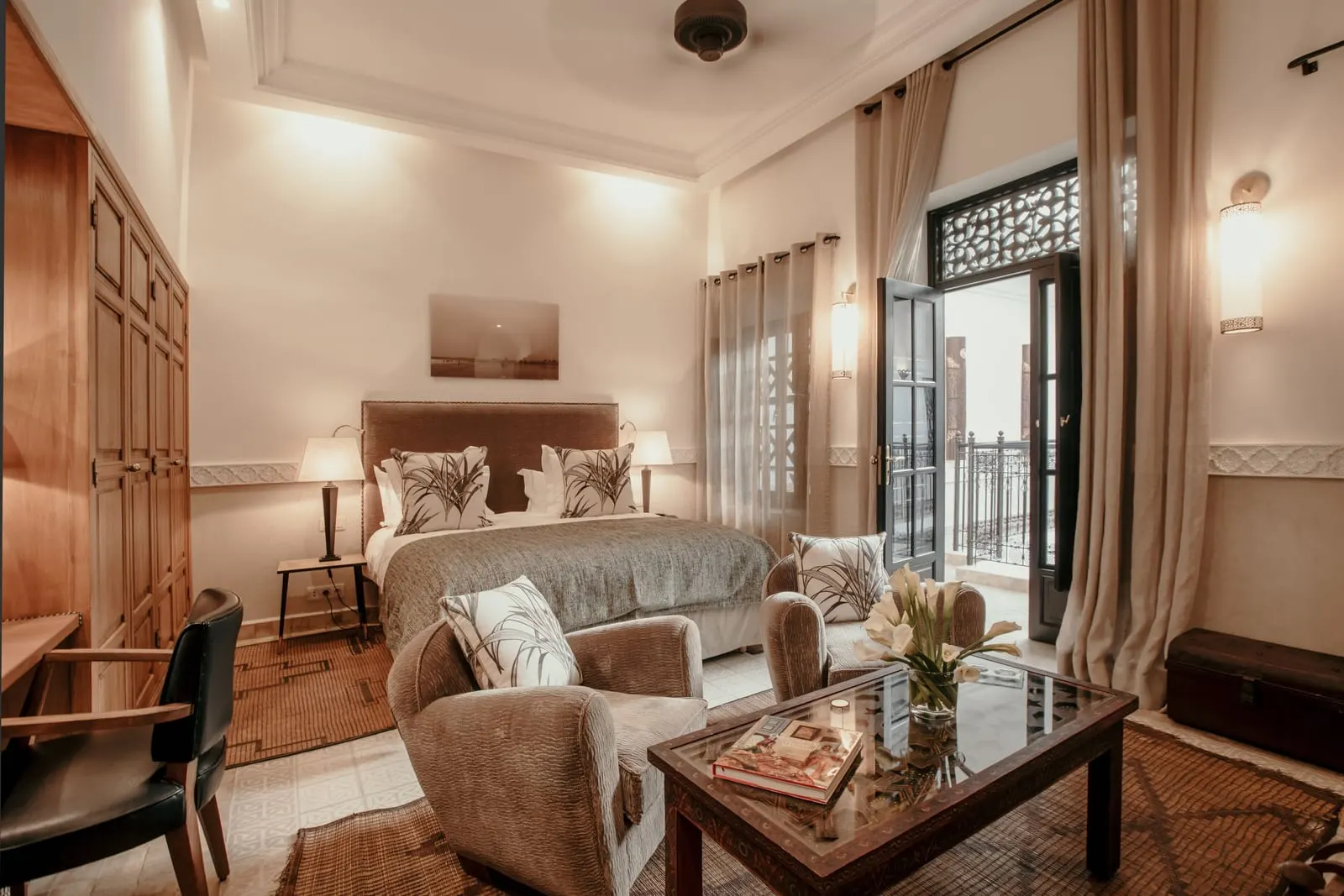 Junior Suite at La Villa des Orangers: a double bed, two armchairs around a glass coffee table and tall doors opening to a railing.