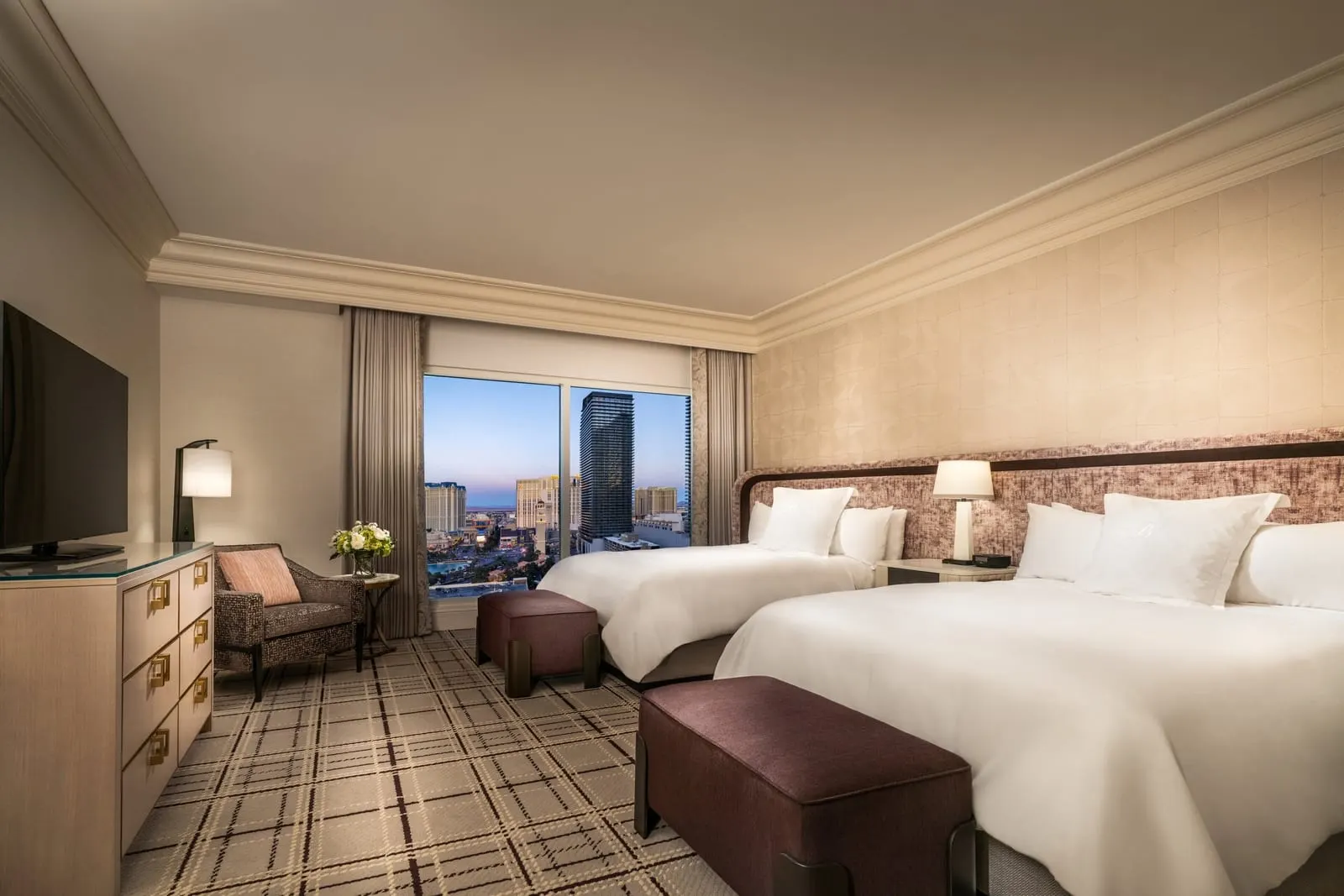 Bellagio Two Queen Suite at Bellagio: two queen beds with a bench at the foot of each, an armchair by the window and a chest of drawers under a television