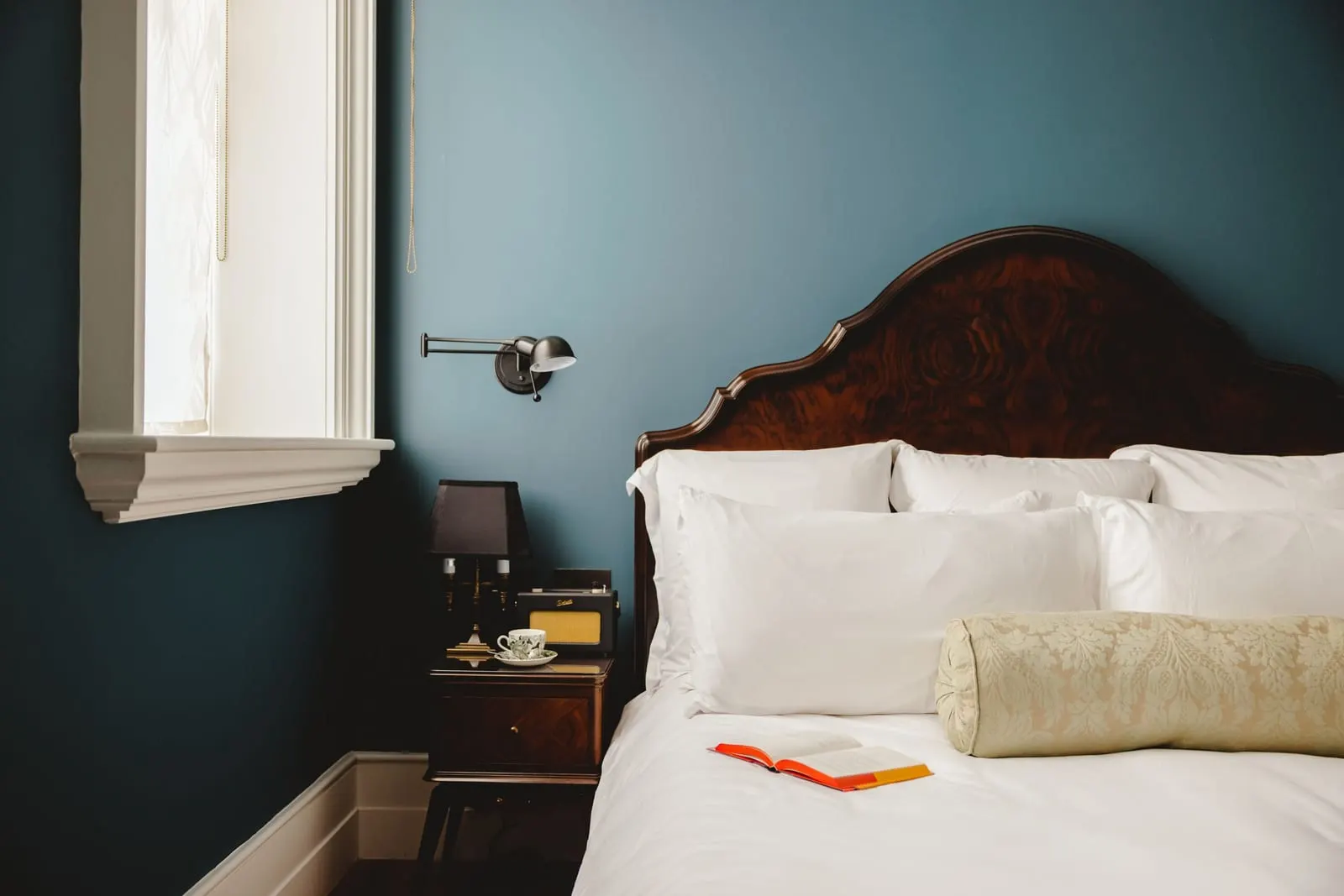 Accessible room at The Ned: the bed with a carved wooden headboard against dark blue walls