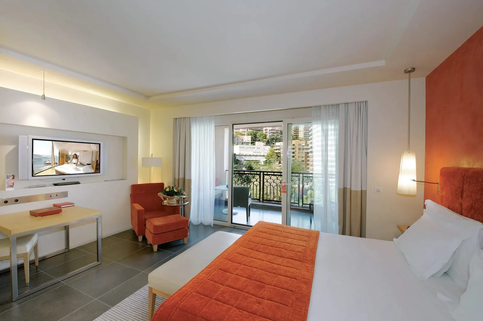 Superior Room with city view at Monte-Carlo Bay Hotel & Resort: the bed, a red armchair and glass doors to the terrace