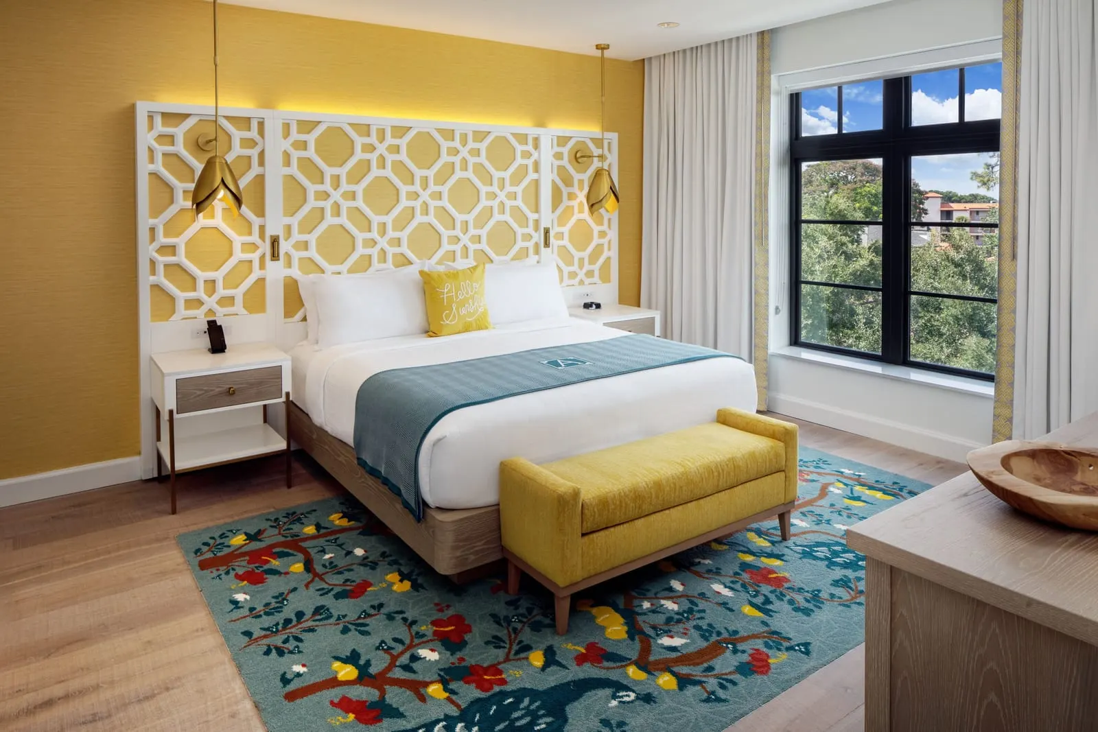 Classic King at The Alfond Inn: a king bed with a white lattice headboard against a yellow wall, a yellow bench at its foot, a peacock-patterned rug and a large window