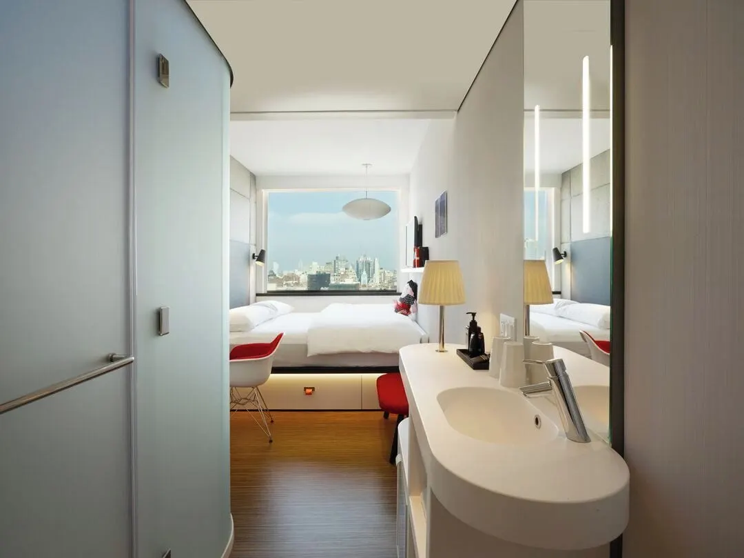 Guest room, 1 King, Premium view at citizenM New York Bowery: looking past the basin and the frosted shower pod to a king bed under a wide window, with a city skyline outside
