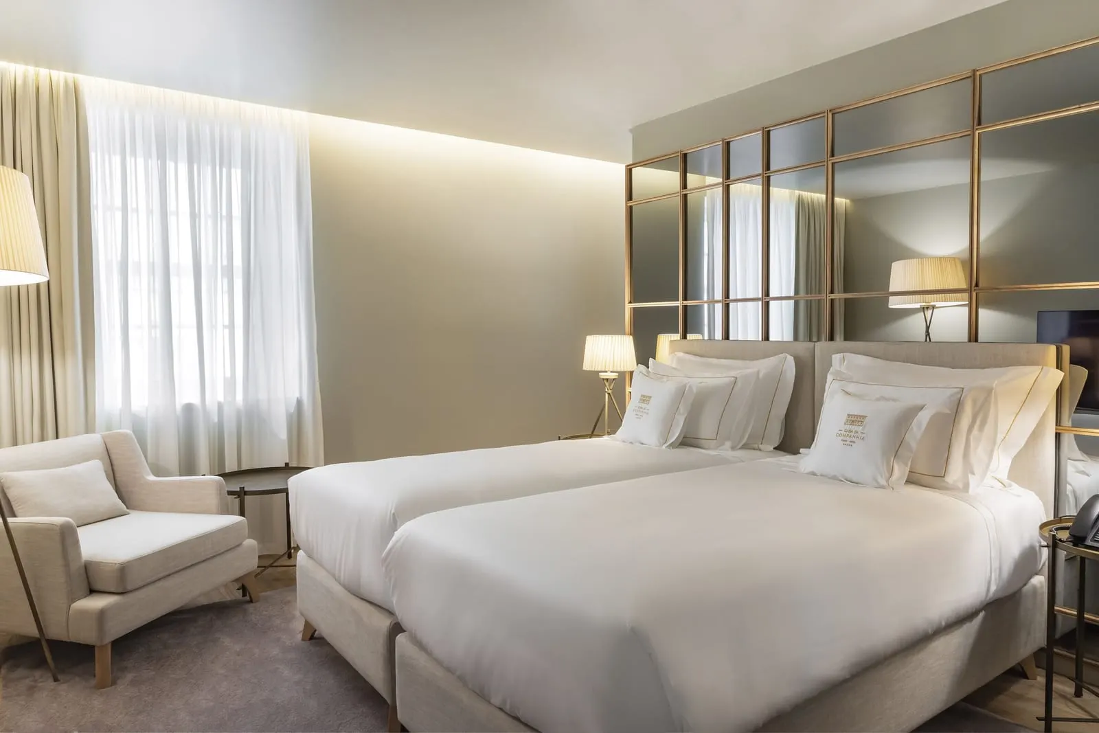 Twin Premium room at Casa da Companhia: two beds against a brass-framed mirror wall, an armchair and a curtained window