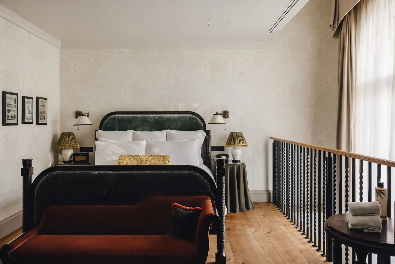 Duplex Suite at The Ned: the bed on the mezzanine, with a red velvet chaise and a balustrade