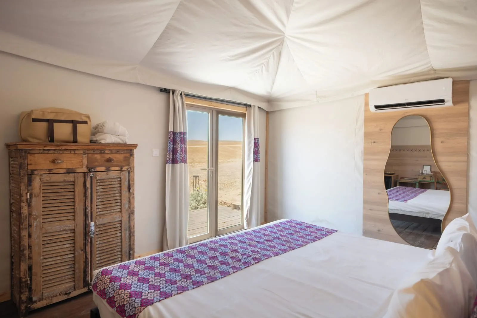 Discovery Tent at Inara Camp: a bed with a purple patterned throw beside a wooden wardrobe, a wall mirror and glass doors under the tent roof.