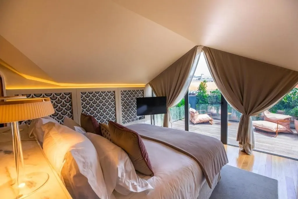 Sublime Suite at Sublime Lisboa: the bed under a sloping ceiling and glass doors to a decked terrace with two loungers