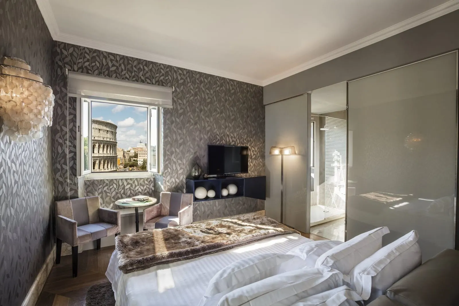 Master Room at Palazzo Manfredi: the bed, two armchairs at a small table and the Colosseum in the window