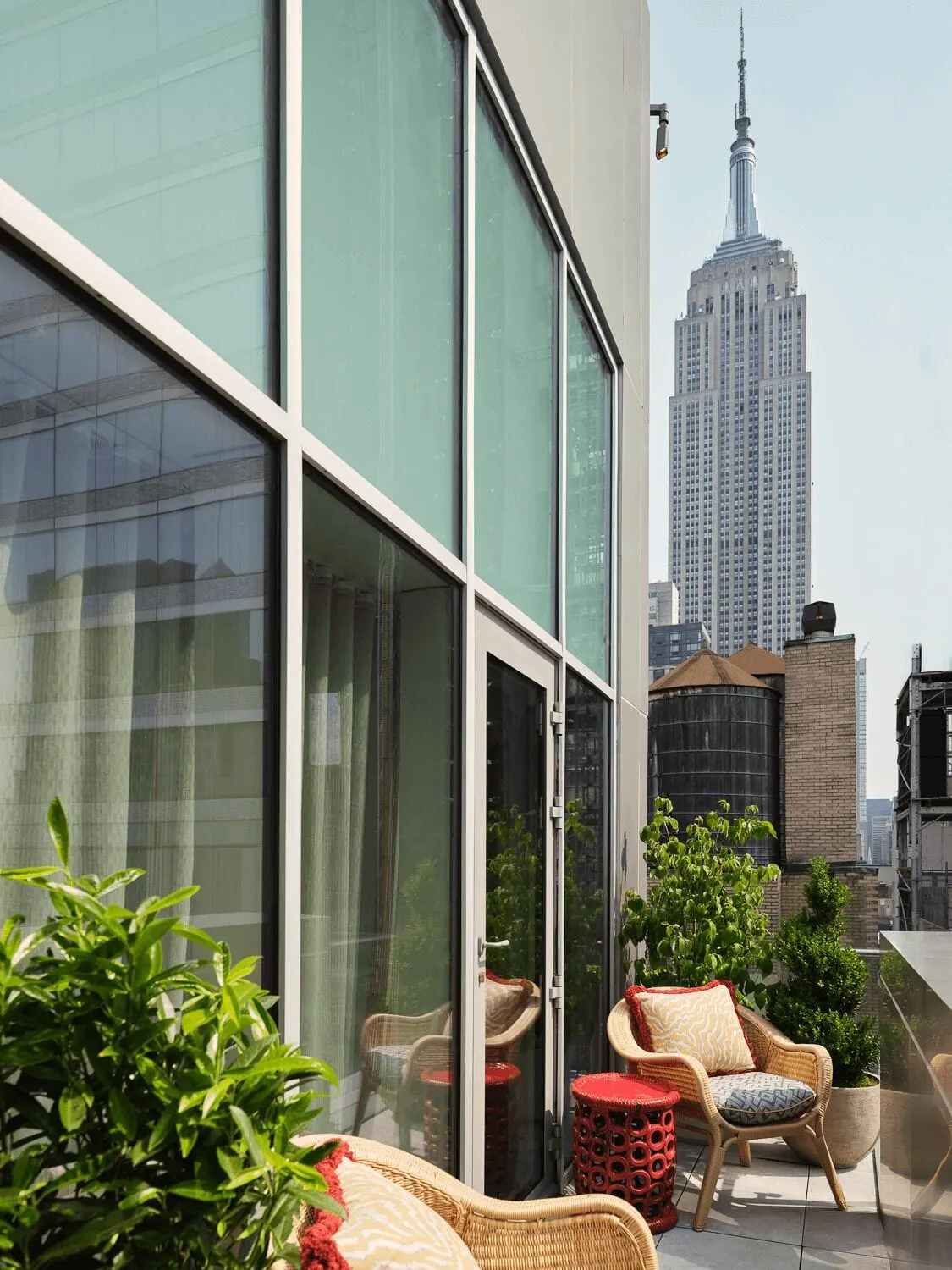 Studio Suite Terrace at The Fifth Avenue Hotel: a terrace with wicker armchairs, a red side table and potted plants beside tall glass doors